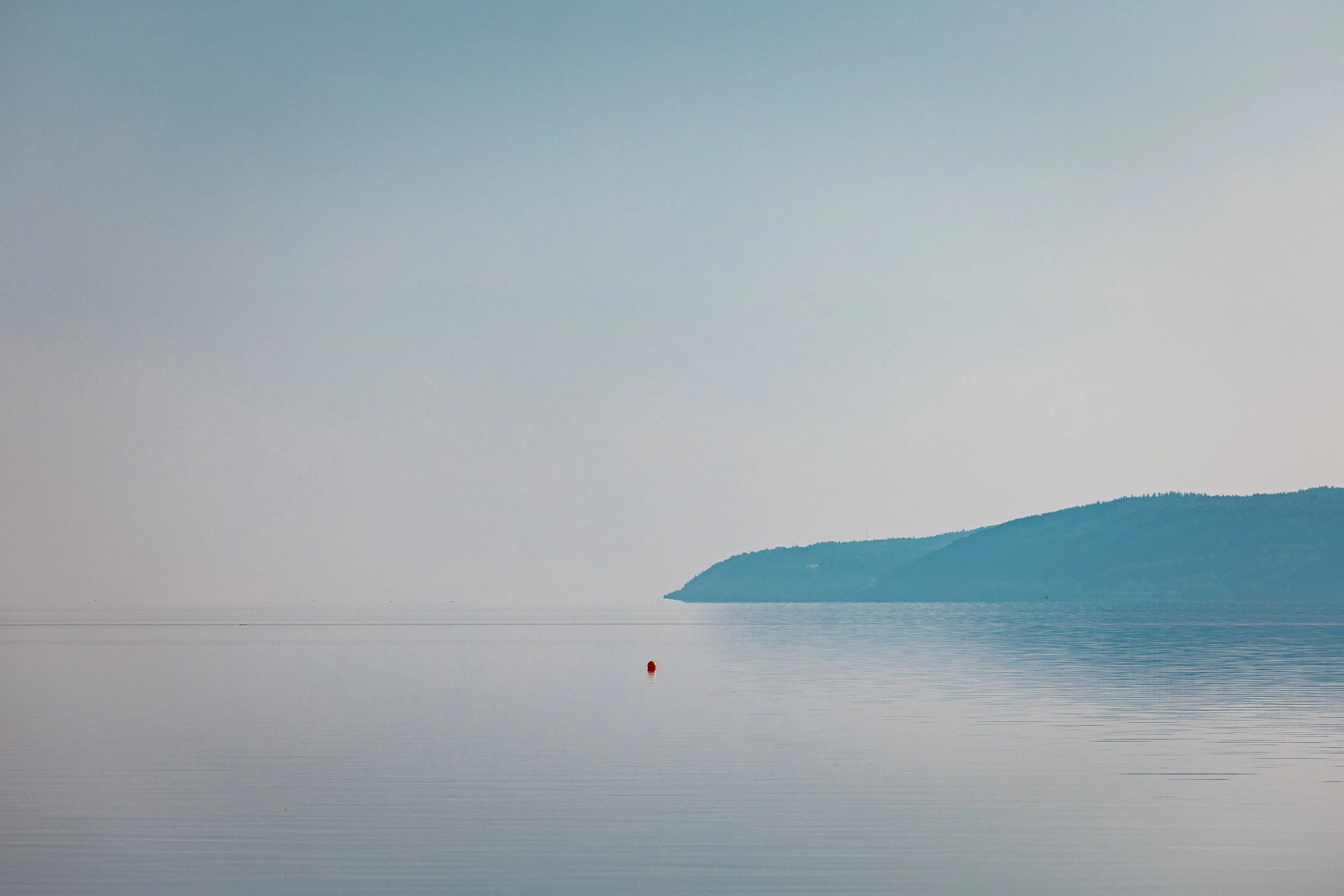Calm body of water with a distant shoreline and a small red buoy floating on the surface.