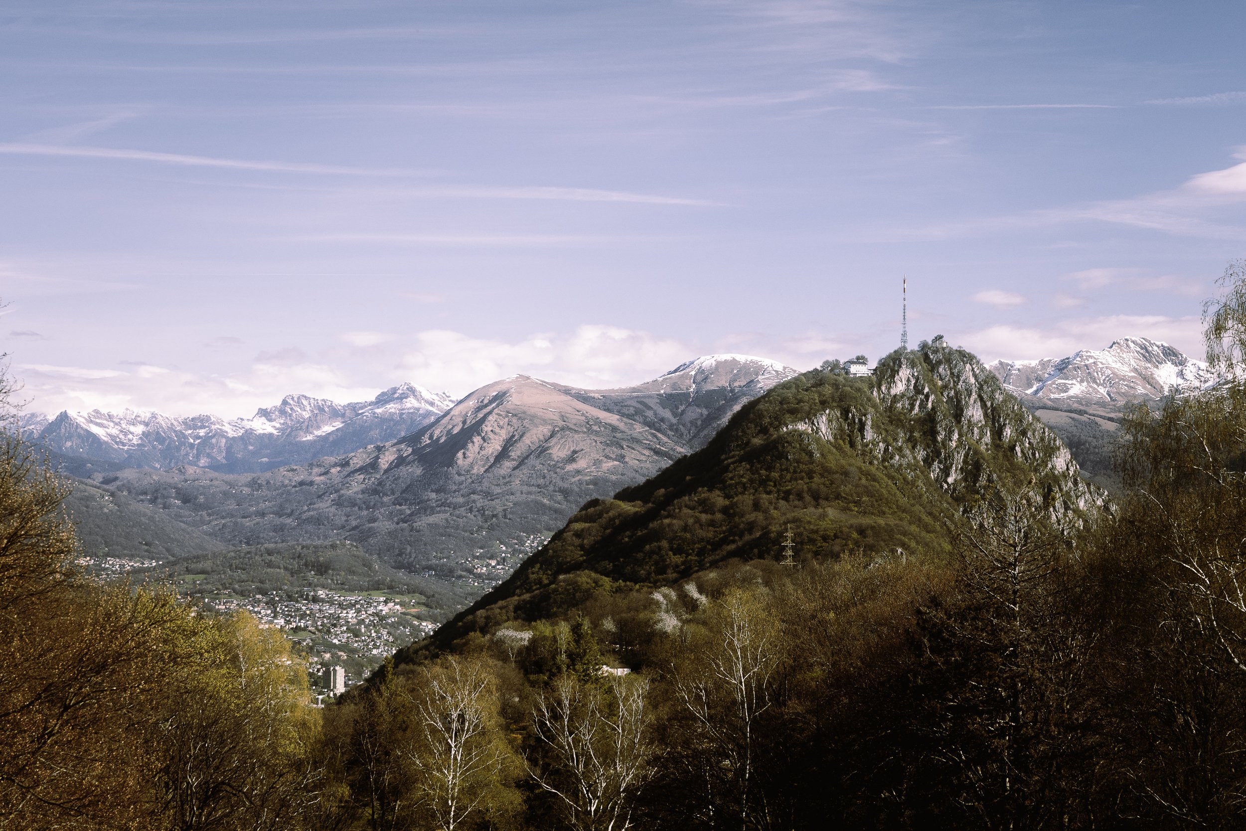 Vuoristomaisema, joissa on lehvästön alla kaupunki ja taivaalla pilviä ja vuoria, joilla on lumiset huiput.