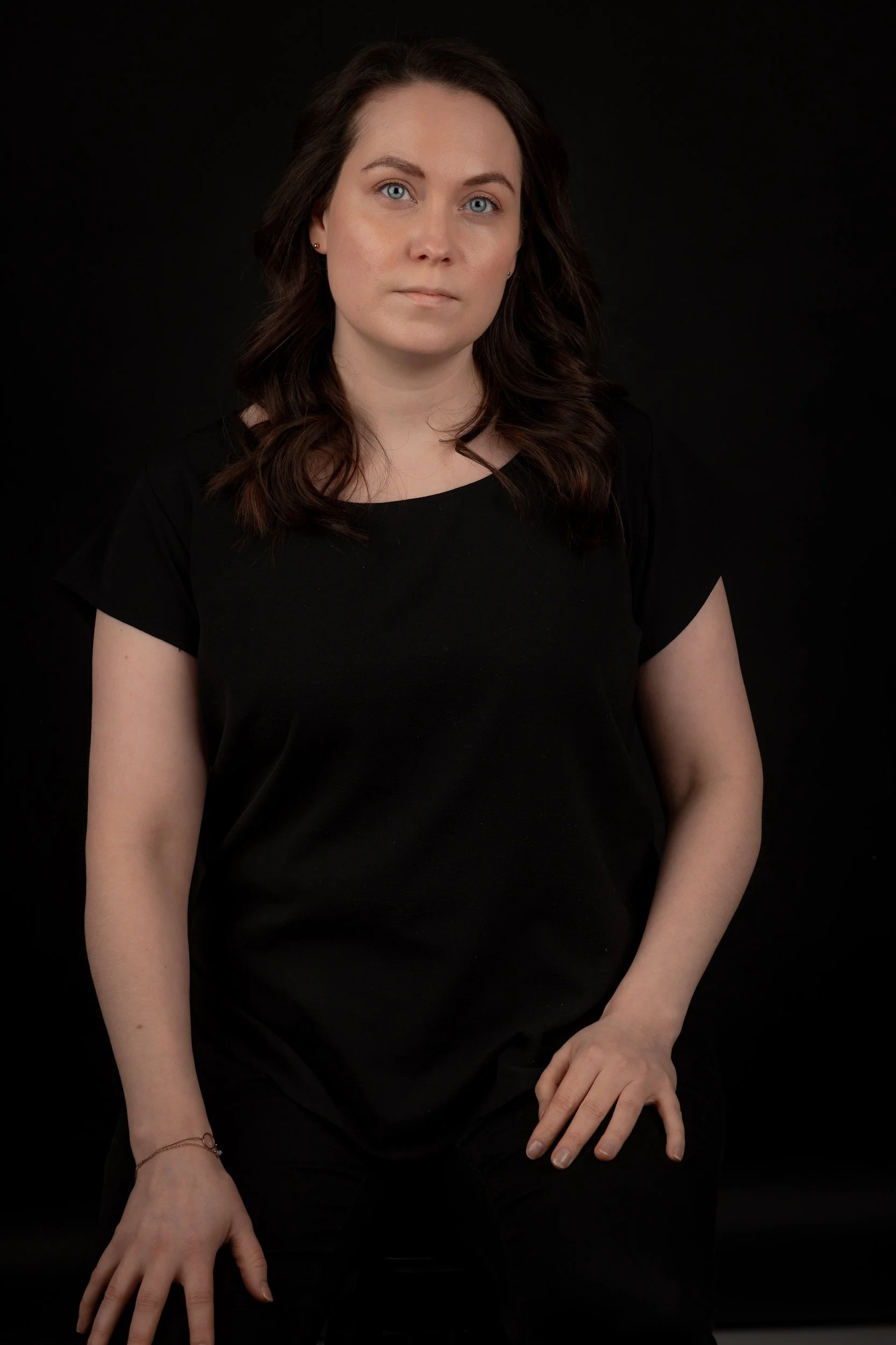 Portrait of a woman with dark brown wavy hair, wearing a black shirt, against a black background.