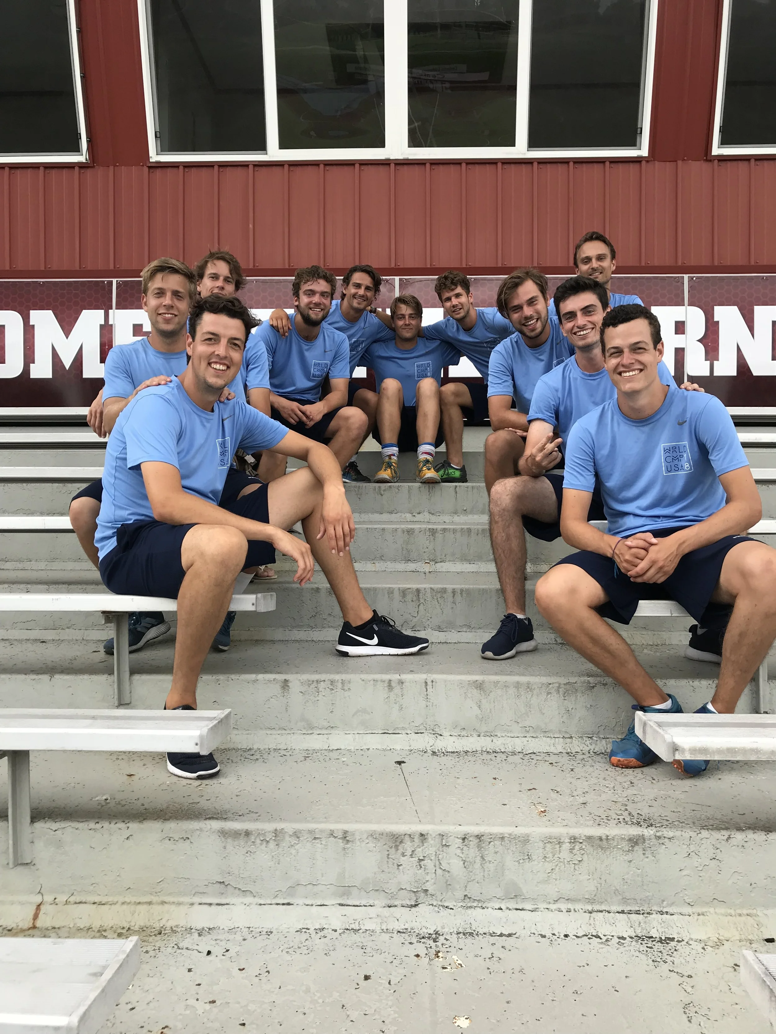 Een groep jonge mannen in blauwe sportkleding zittend en knielend op de tribune van een sportstadion.
