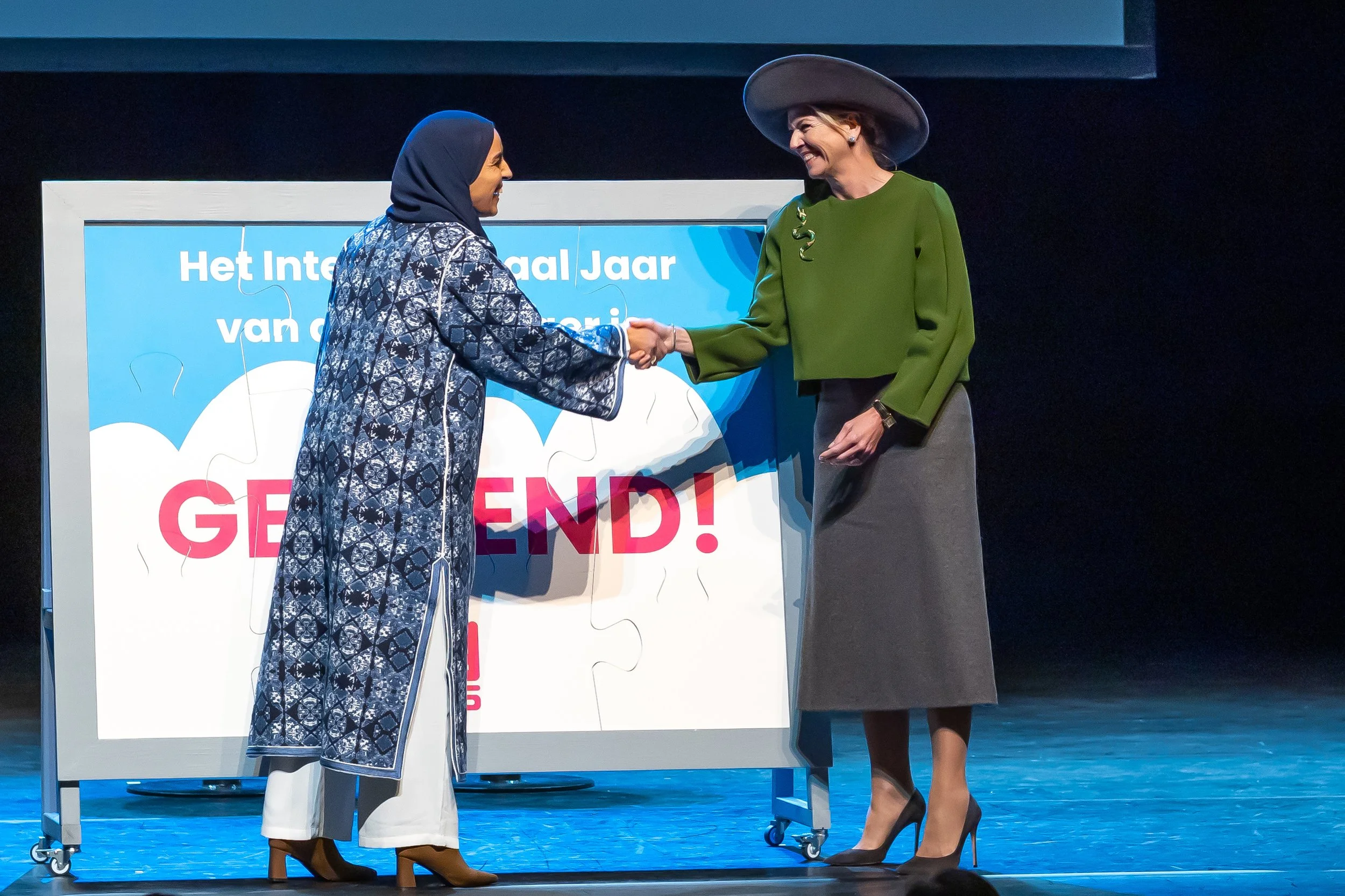 Koningin Maxima en directrice Vrijwilligerswerk Laila samen op het podium elkaar de handschuddend