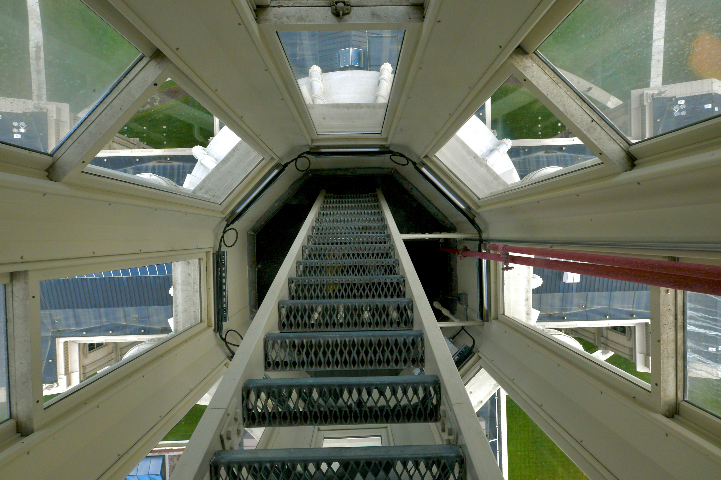 image from the top of a ladder or stair looking downward. The curving dome and capitol rooftop and lawn can be seen through tall windows below.