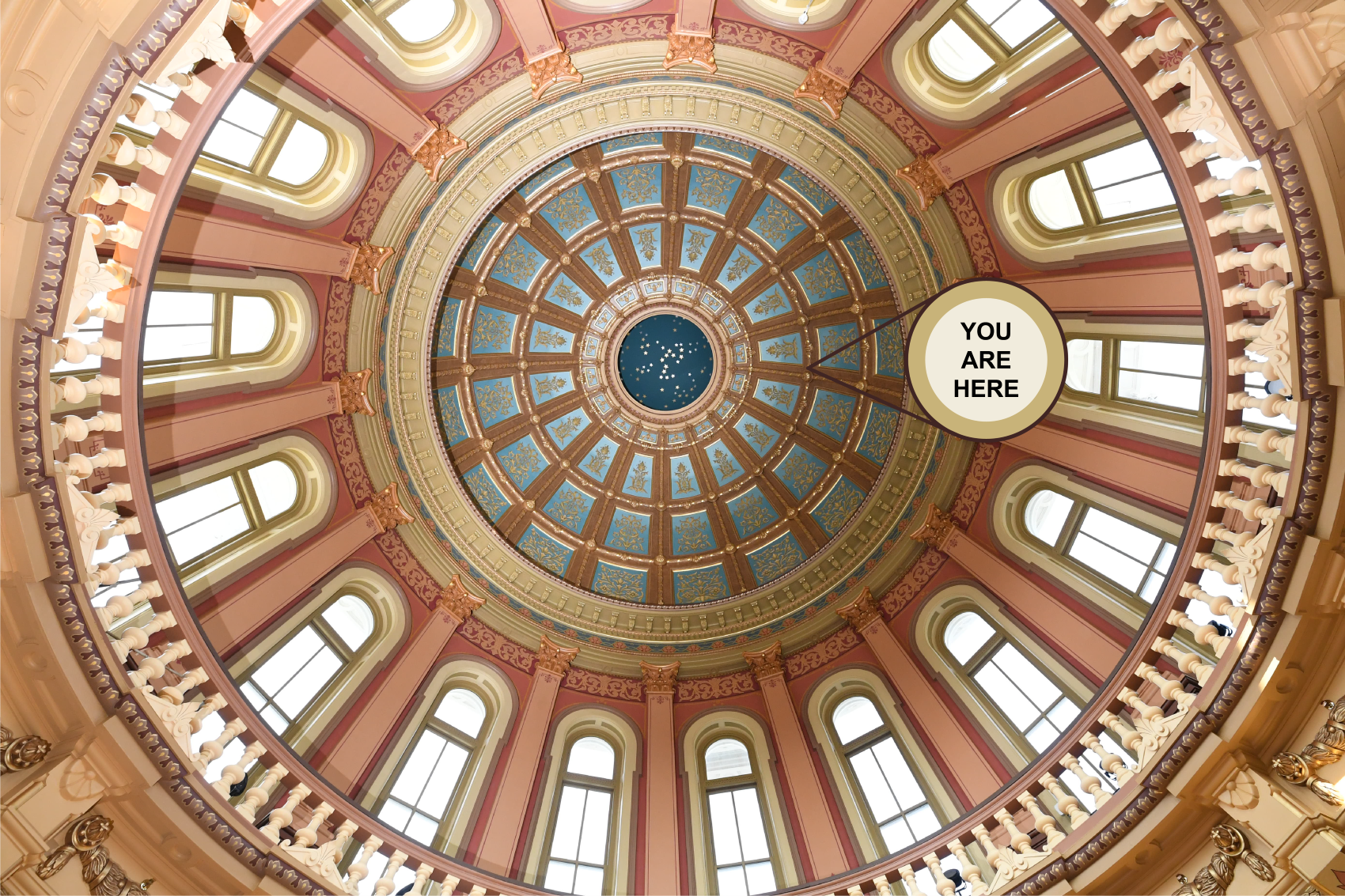 image showing partial views of the Michigan State Capitol dome interior with ornate gold detailing and arched windows, and a "you are here" arrow overlayed pointing toward the top of the rotunda dome.