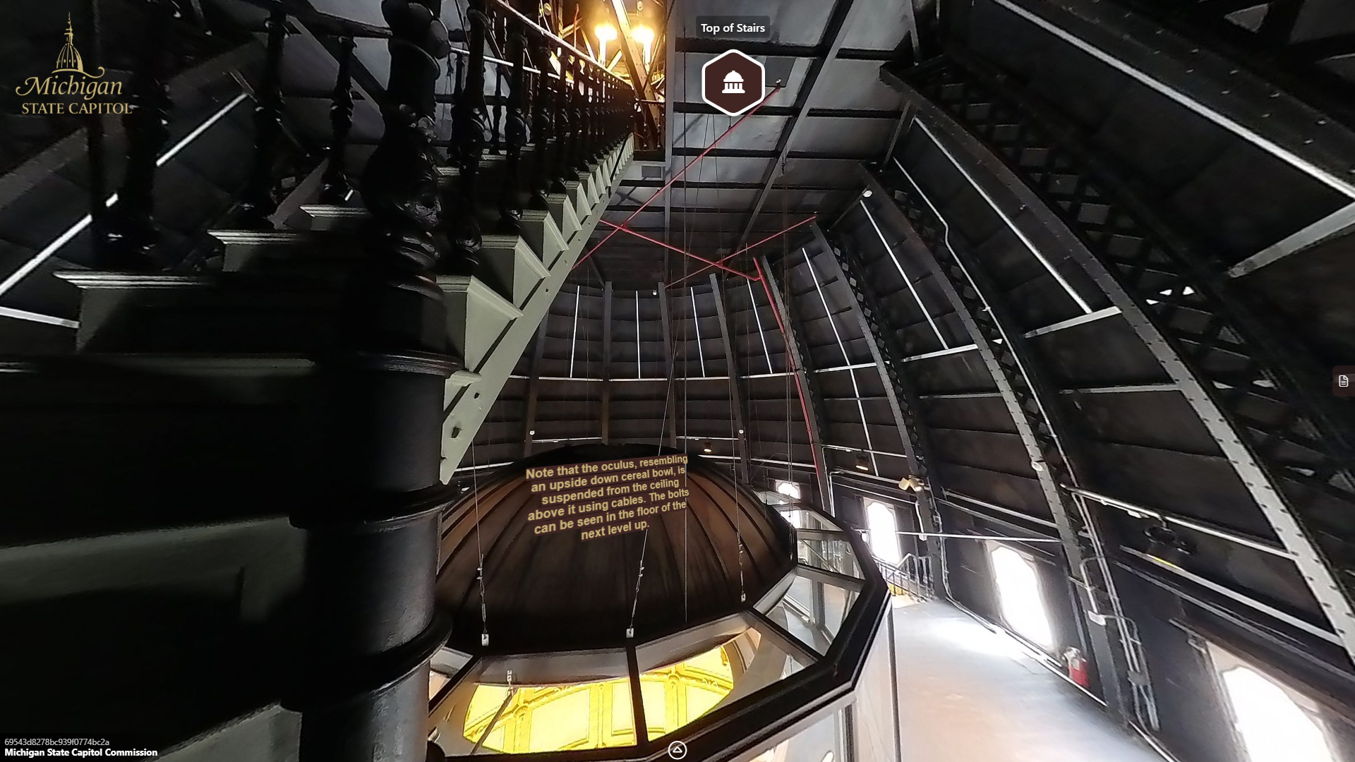 image of a large open space with windows and metal walls and trusses. A metal staircase leads upward on the left side above a circular glass and metal enclosure below.