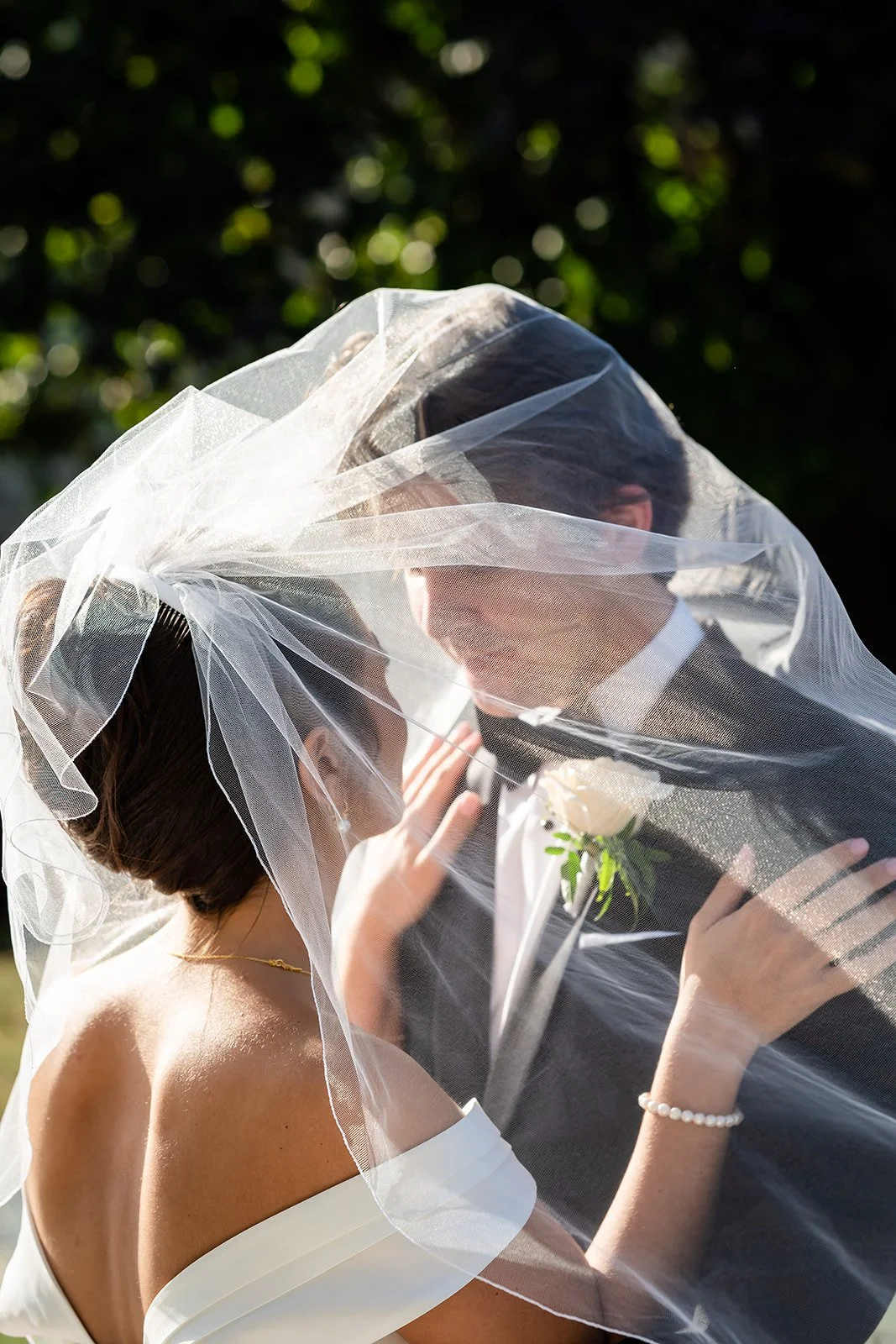 man and woman looking at each other under a veil in wedding attire