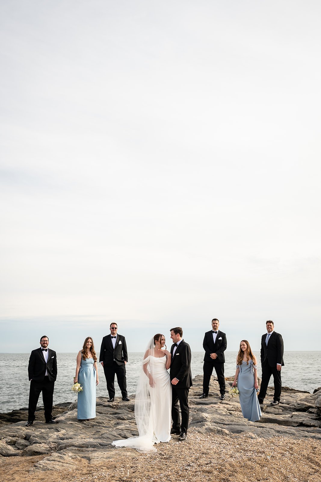 Three Women and Five Men standing on rocks in wedding attire posing around the bride and groom