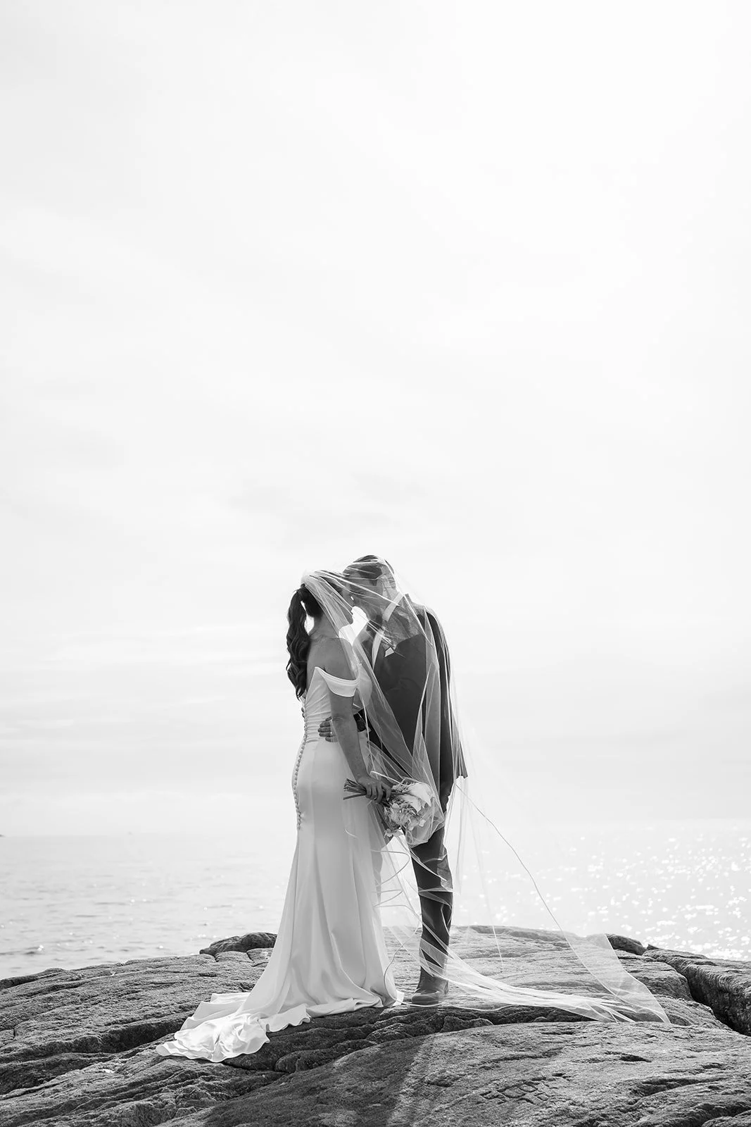 Woman and Man kissing under a veil on rocks in wedding attire