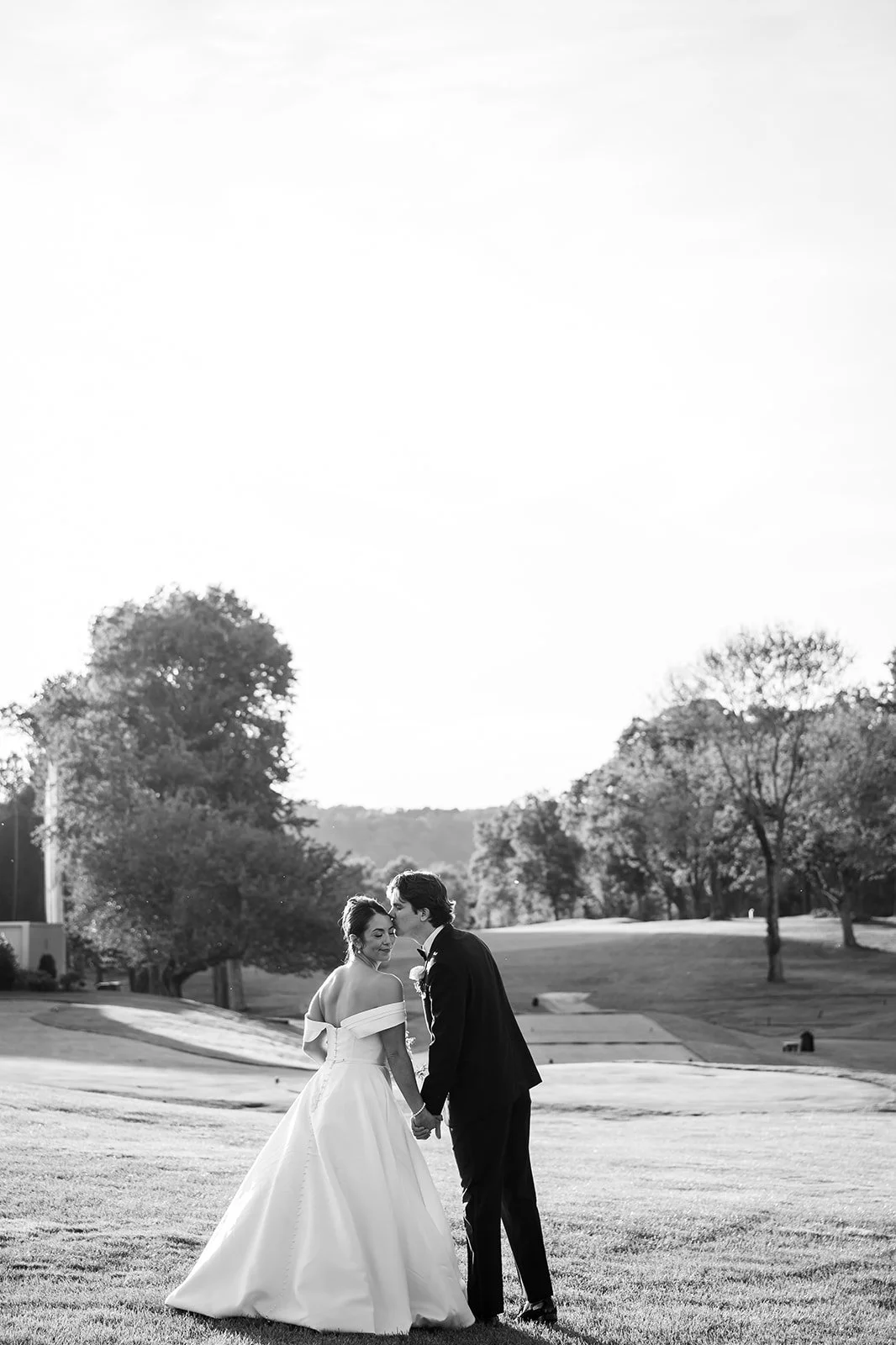 Man in black tux kissing woman on forehead in a white satin wedding dress