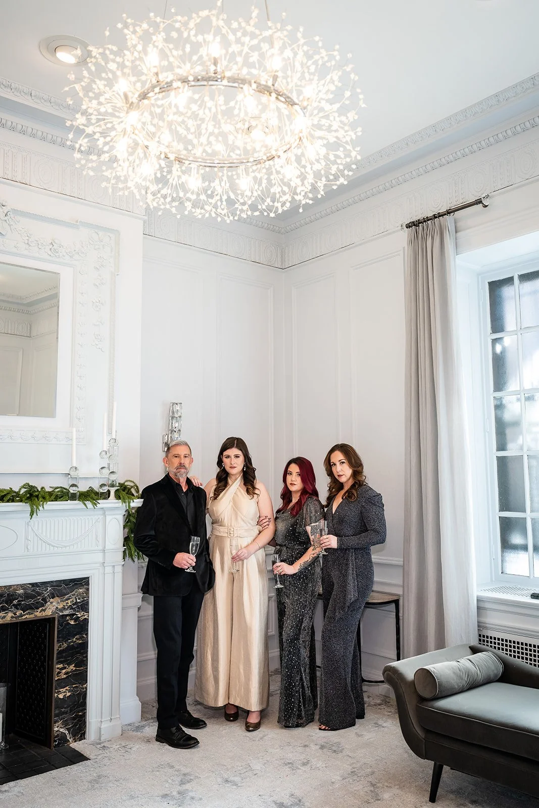 three women and one man standing holding wine glasses posed in front of fireplace and couch