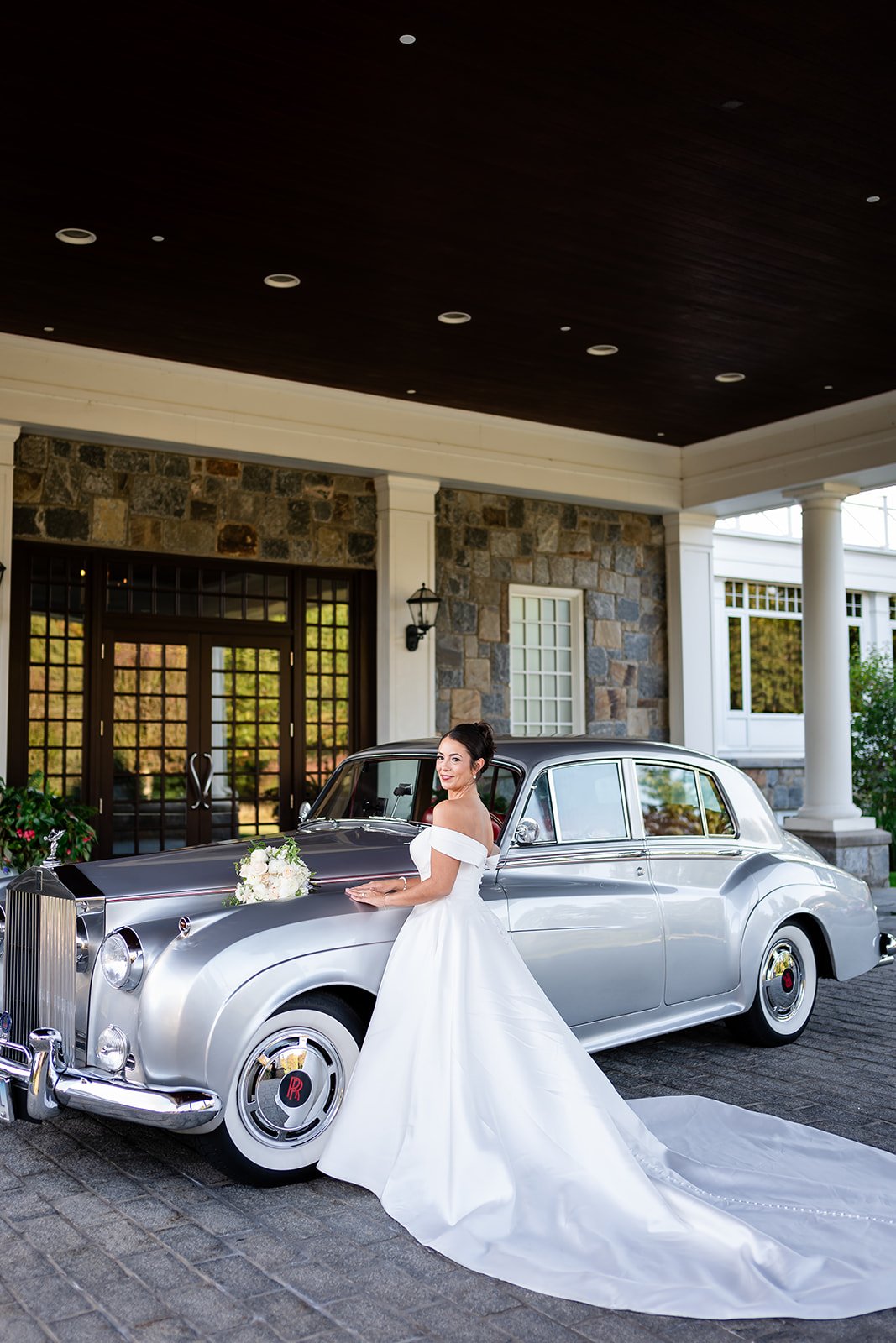 woman in white satin wedding dress standing in front of silver Rolls Royce
