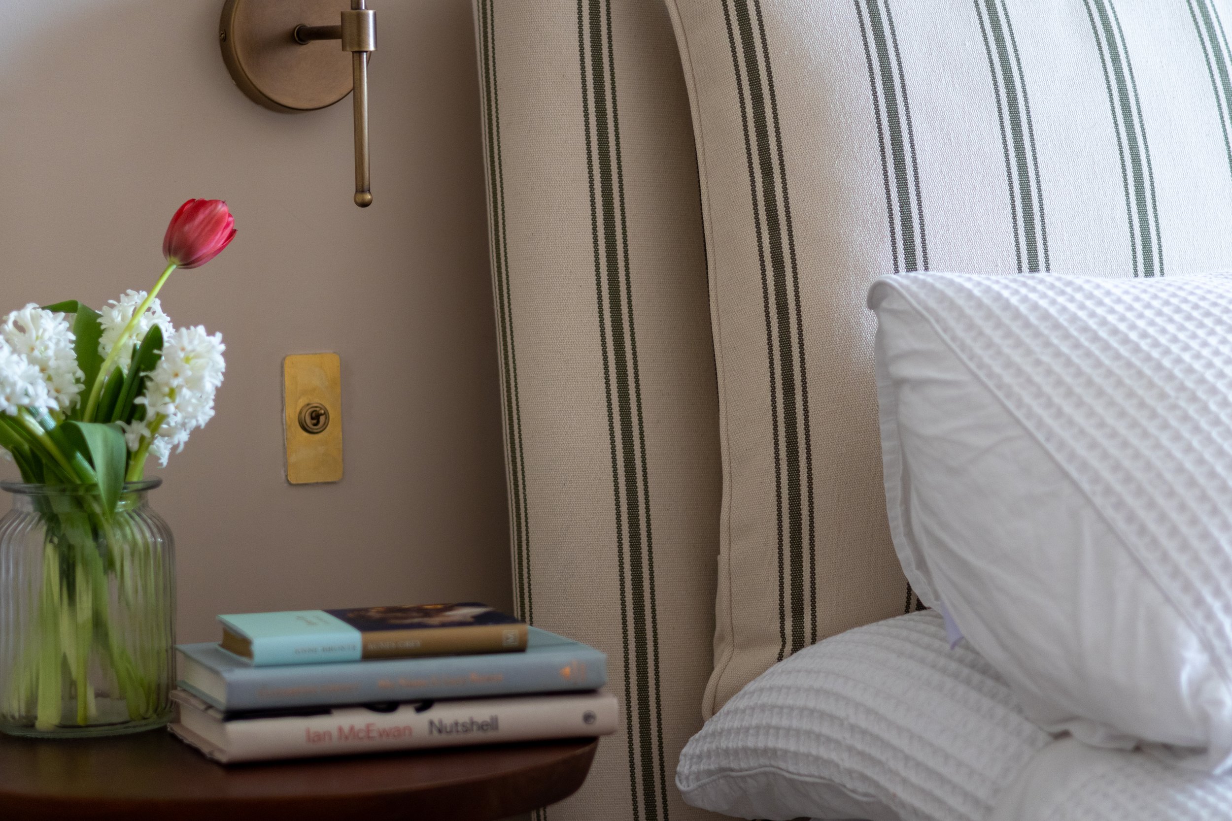 Cream and olive striped headboard beside a bobbin-leg table with tulips and stacked books