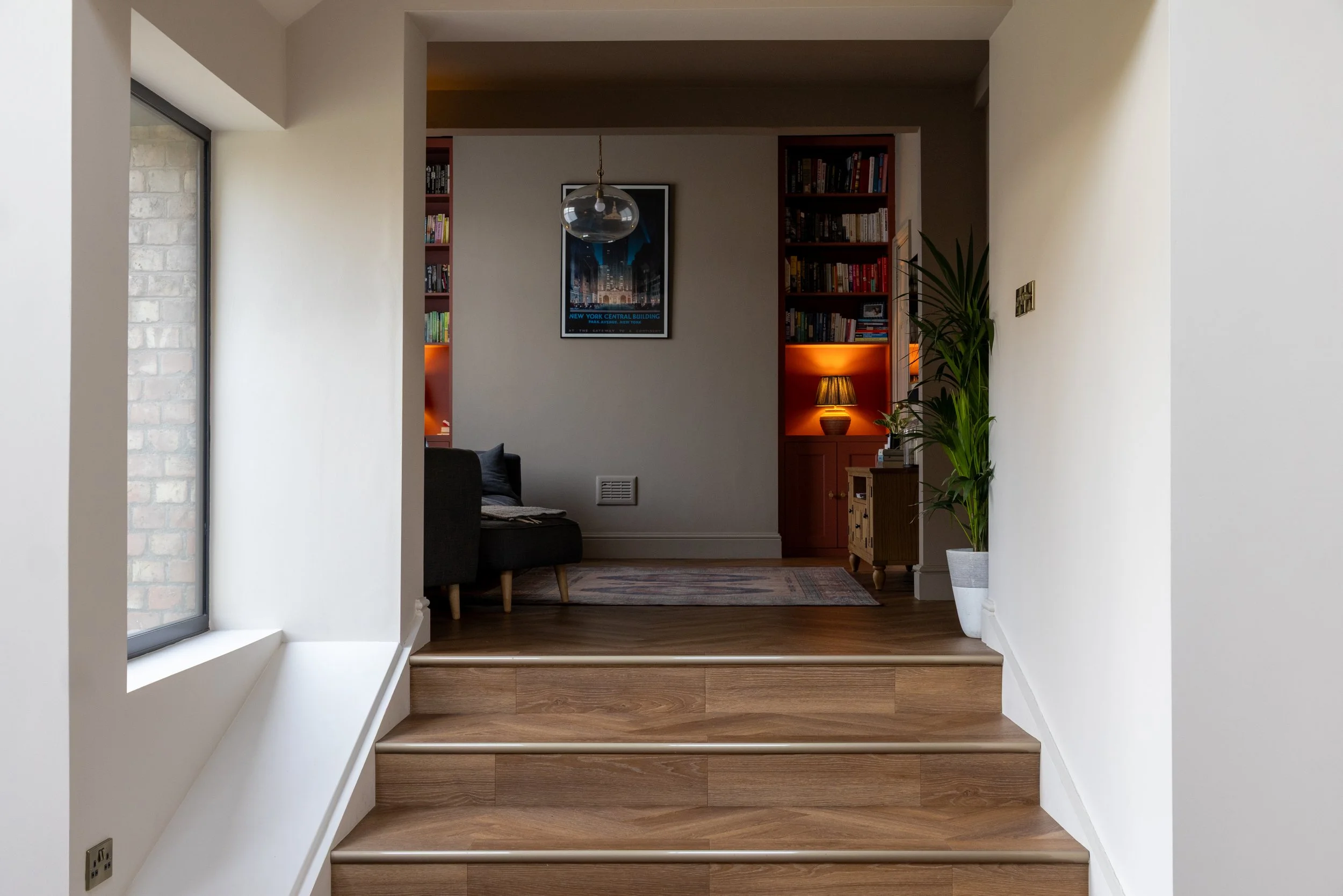 View through to a snug with terracotta bookshelves and a grey sofa, seen from a raised hallway