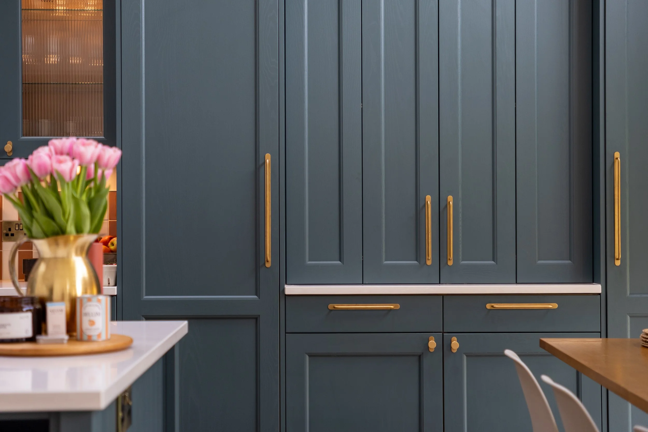 Close-up of teal shaker cabinetry with long brass bar handles and knob pulls