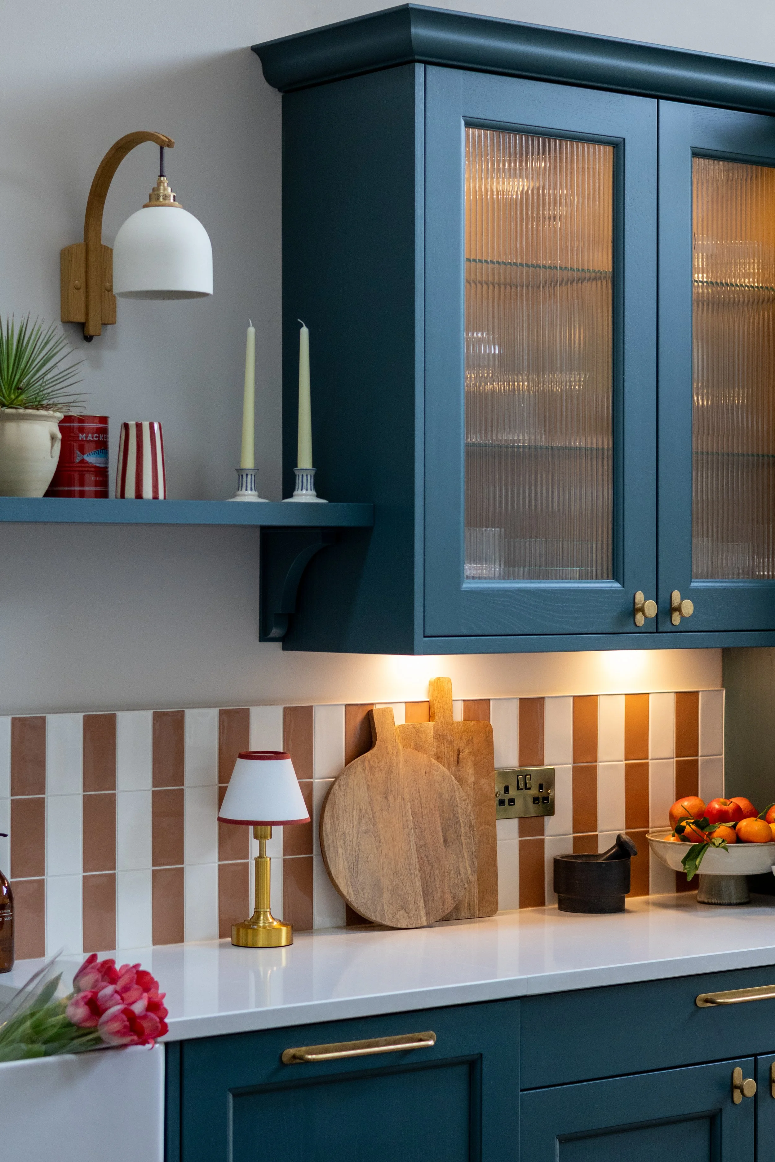 Teal kitchen cabinetry with glass-fronted cupboard, chopping boards and striped tile splashback