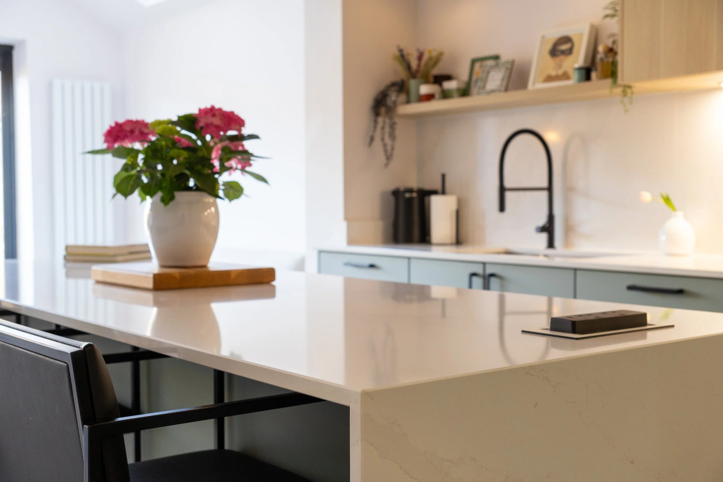 Kitchen island with hydrangea display, open shelving and matte black arched tap in the background
