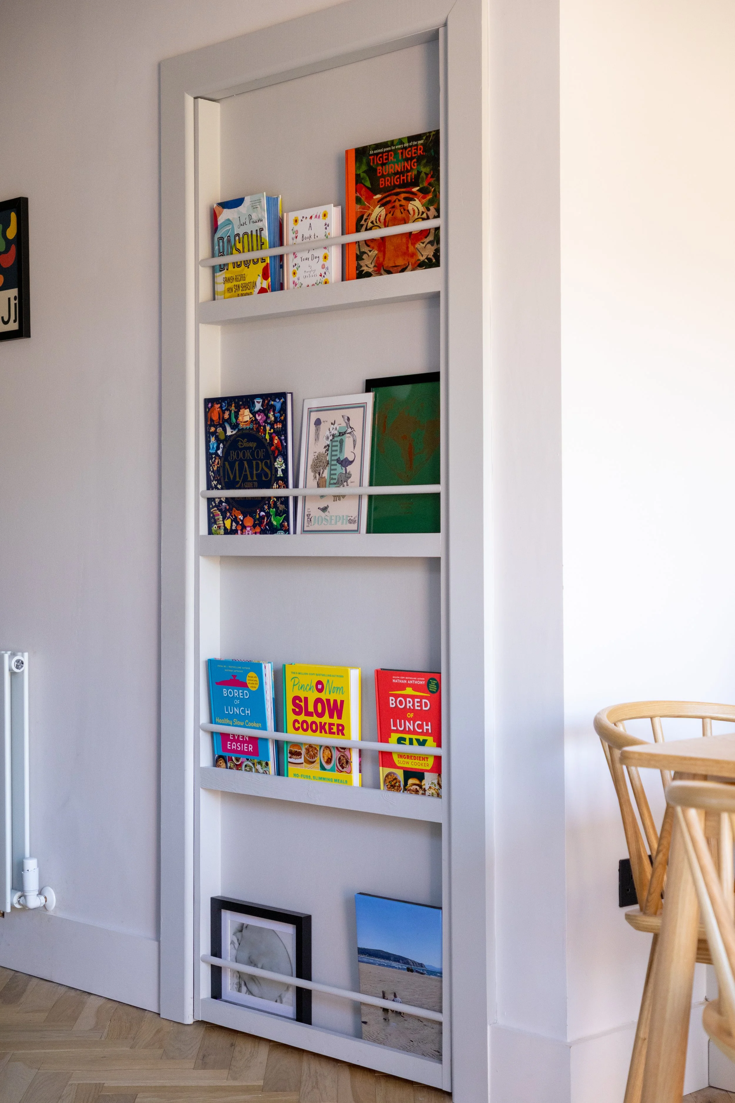 Narrow built-in bookshelf with cookbooks, children's books and framed prints