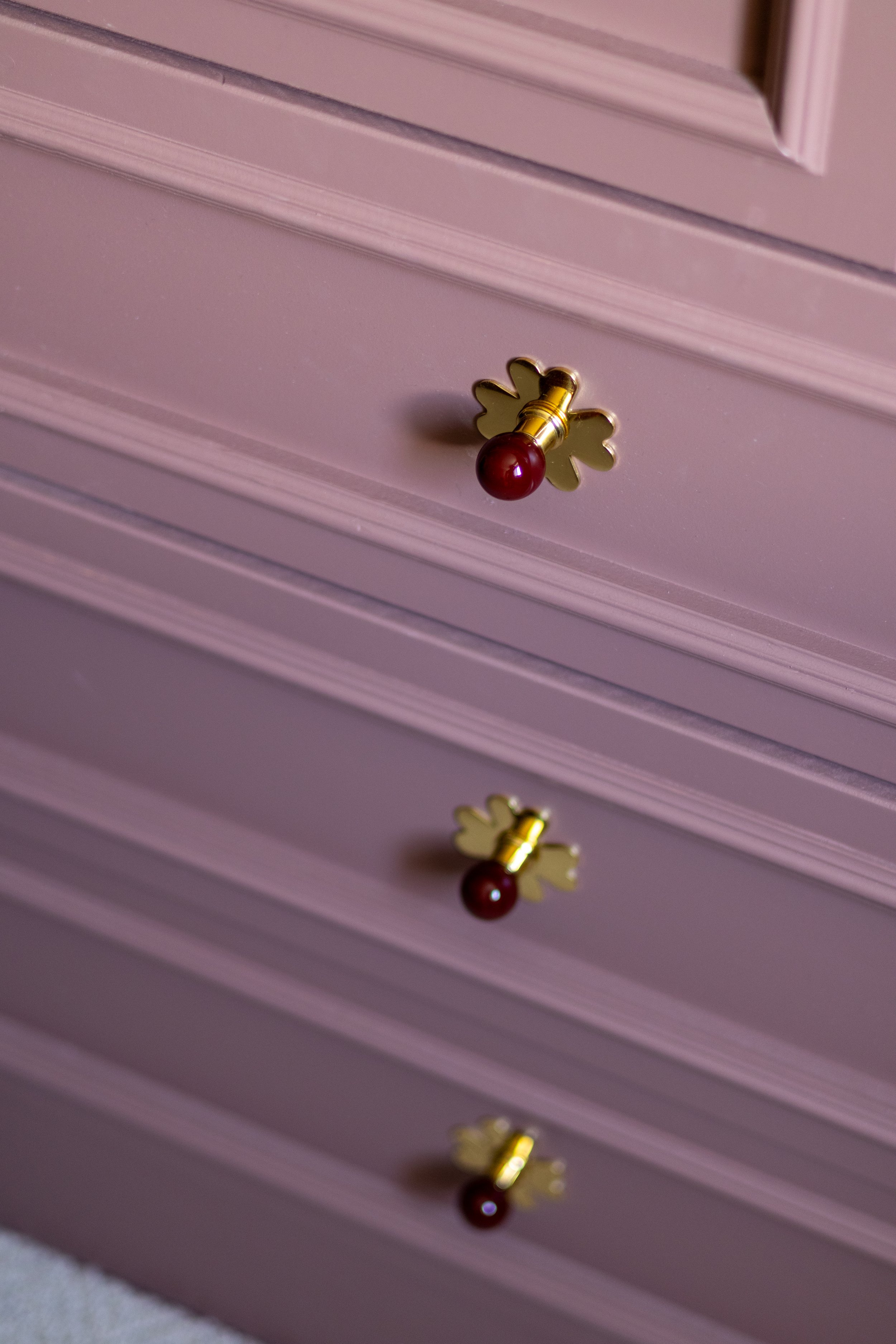 Close-up of brass clover-shaped drawer pulls with deep red glass detailing