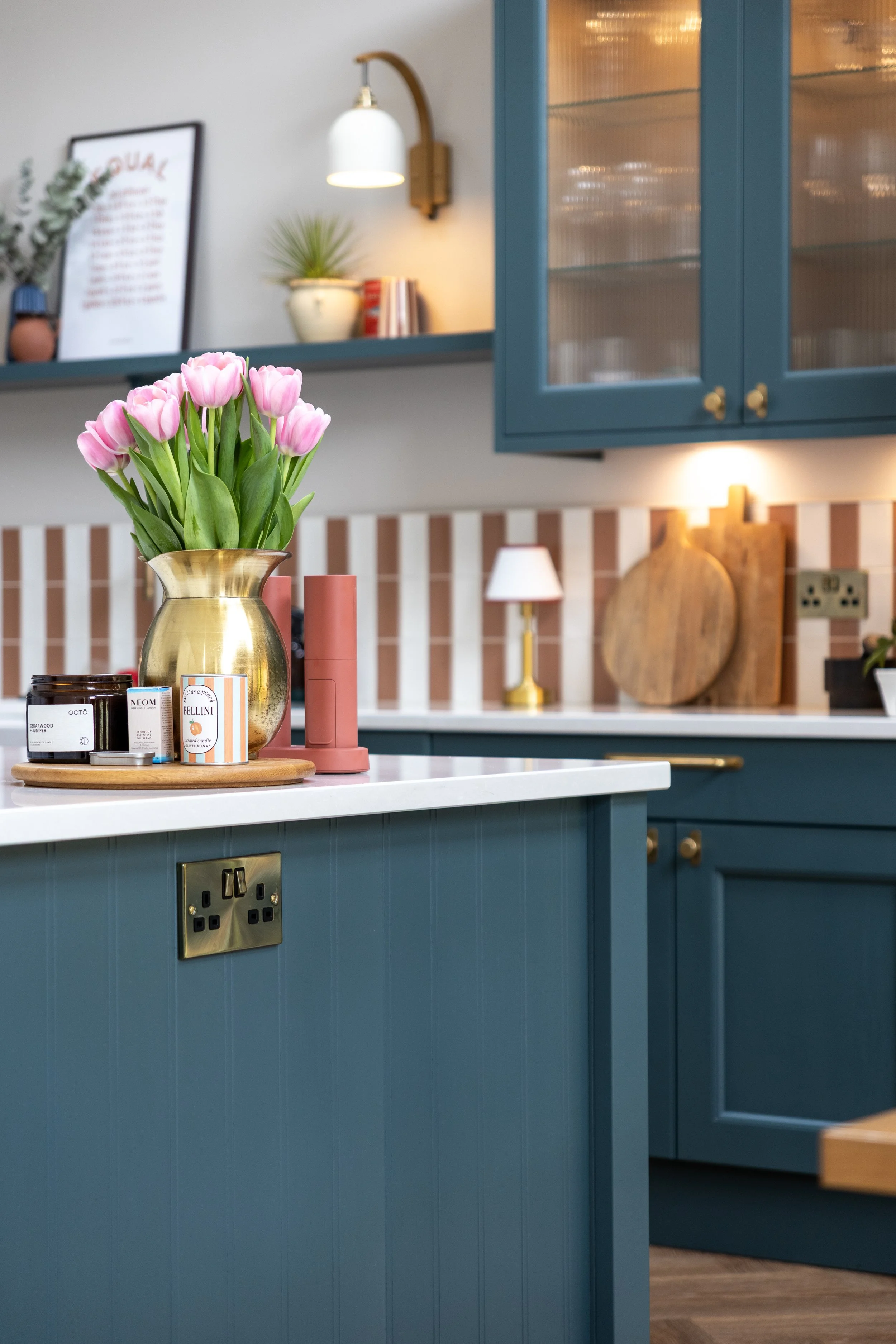 Kitchen island countertop styled with pink tulips in a brass jug, candles and striped tiles behind