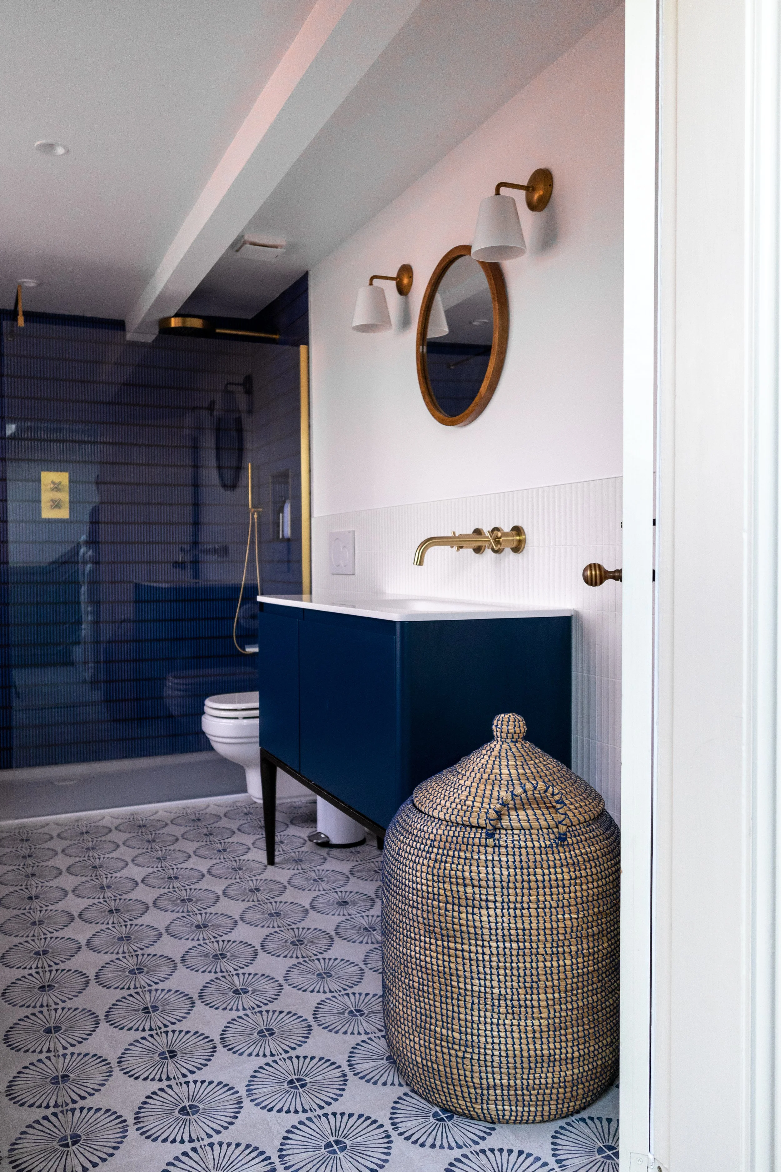 Bathroom with navy vanity, round wooden mirror, wall lights and woven storage basket
