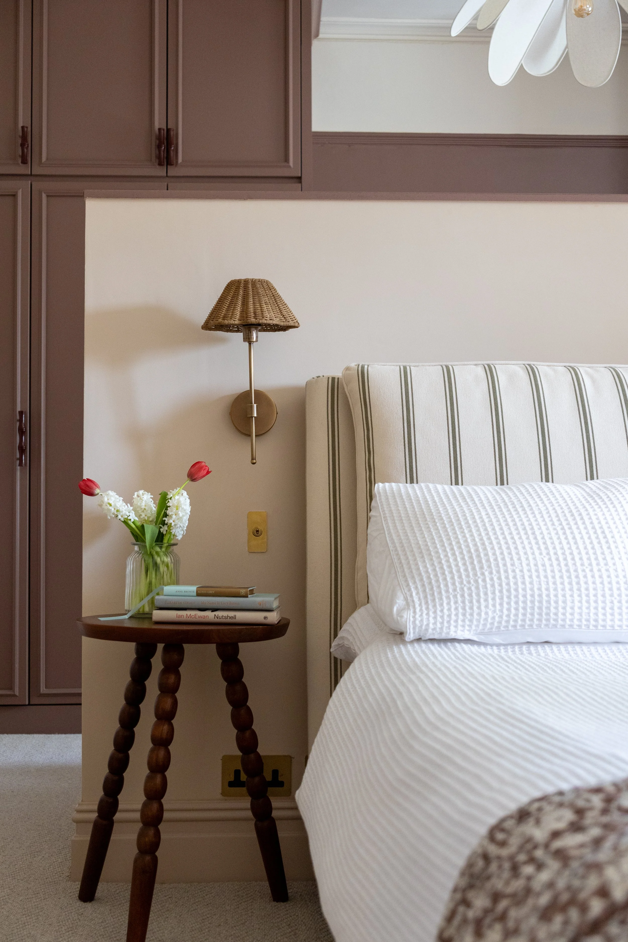 Bedroom corner showing a fitted wardrobe, rattan wall sconce and striped headboard