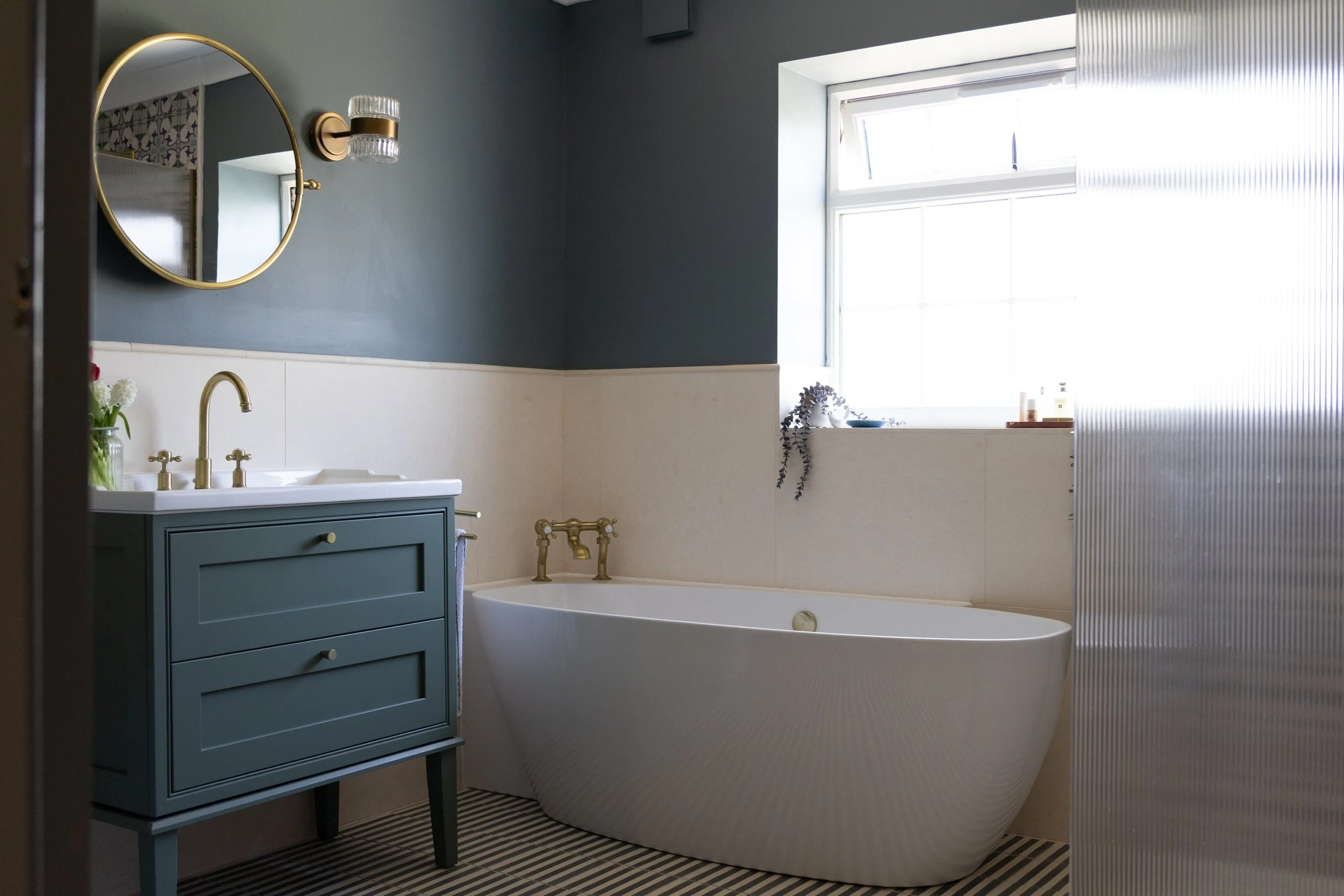 Blue-grey bathroom with freestanding bath, striped tiled floor and teal vanity unit