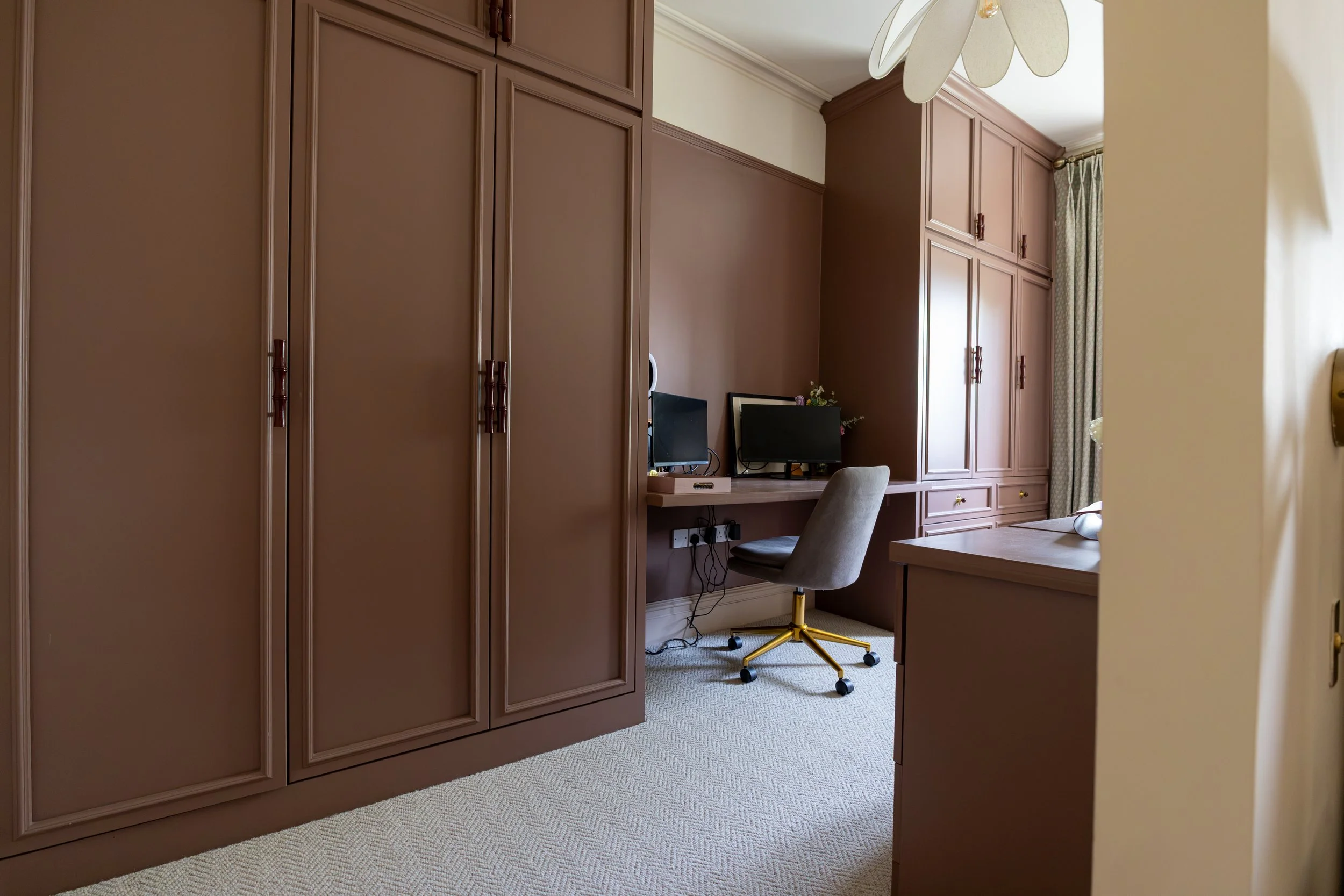 Dusky pink fitted wardrobe with clover brass handles beside a built-in desk workspace