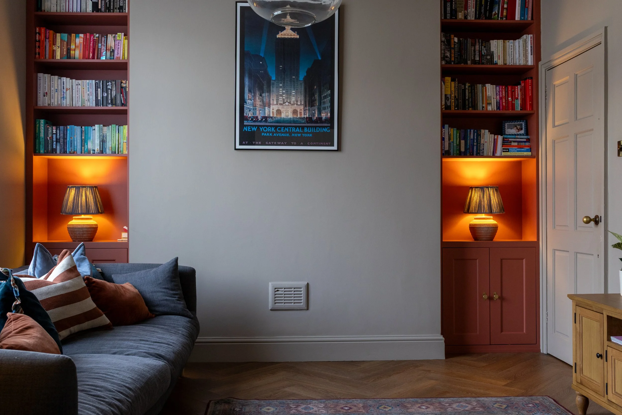 Snug with terracotta built-in alcove bookshelves, glowing lamps either side of a framed print