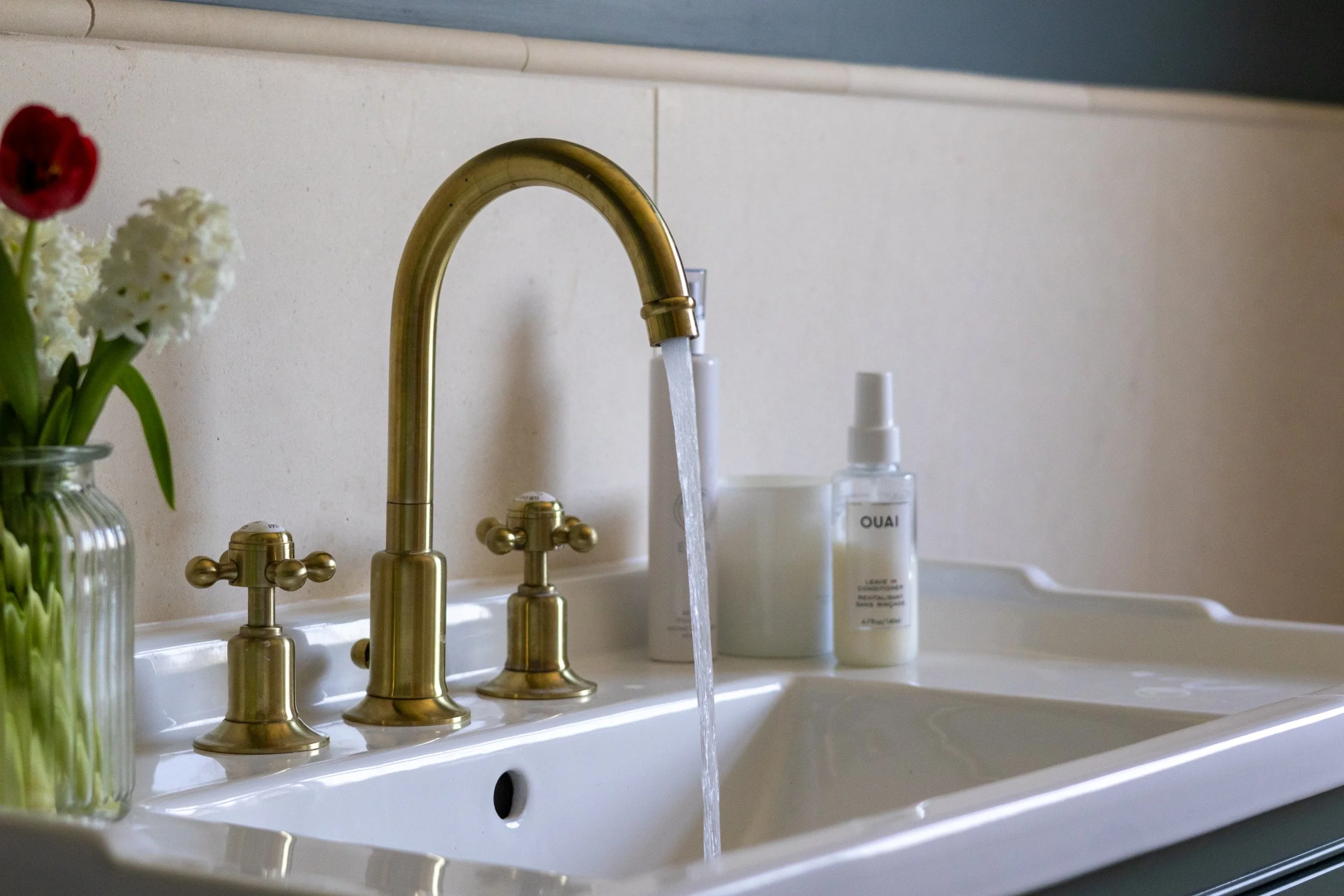 Brass gooseneck basin tap running water beside bathroom toiletries and tulips
