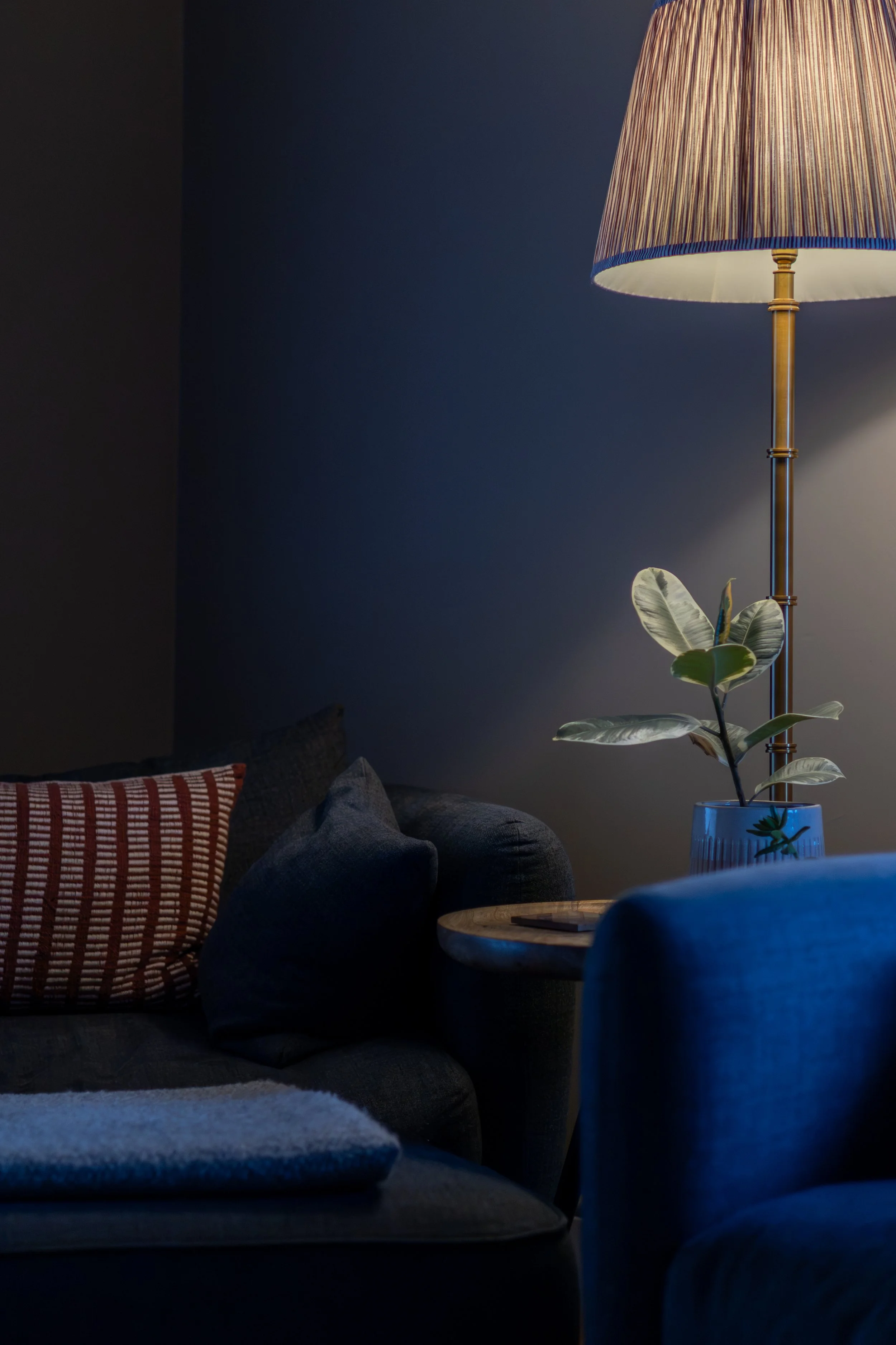 Brass floor lamp with pleated shade beside a potted plant and blue velvet armchair