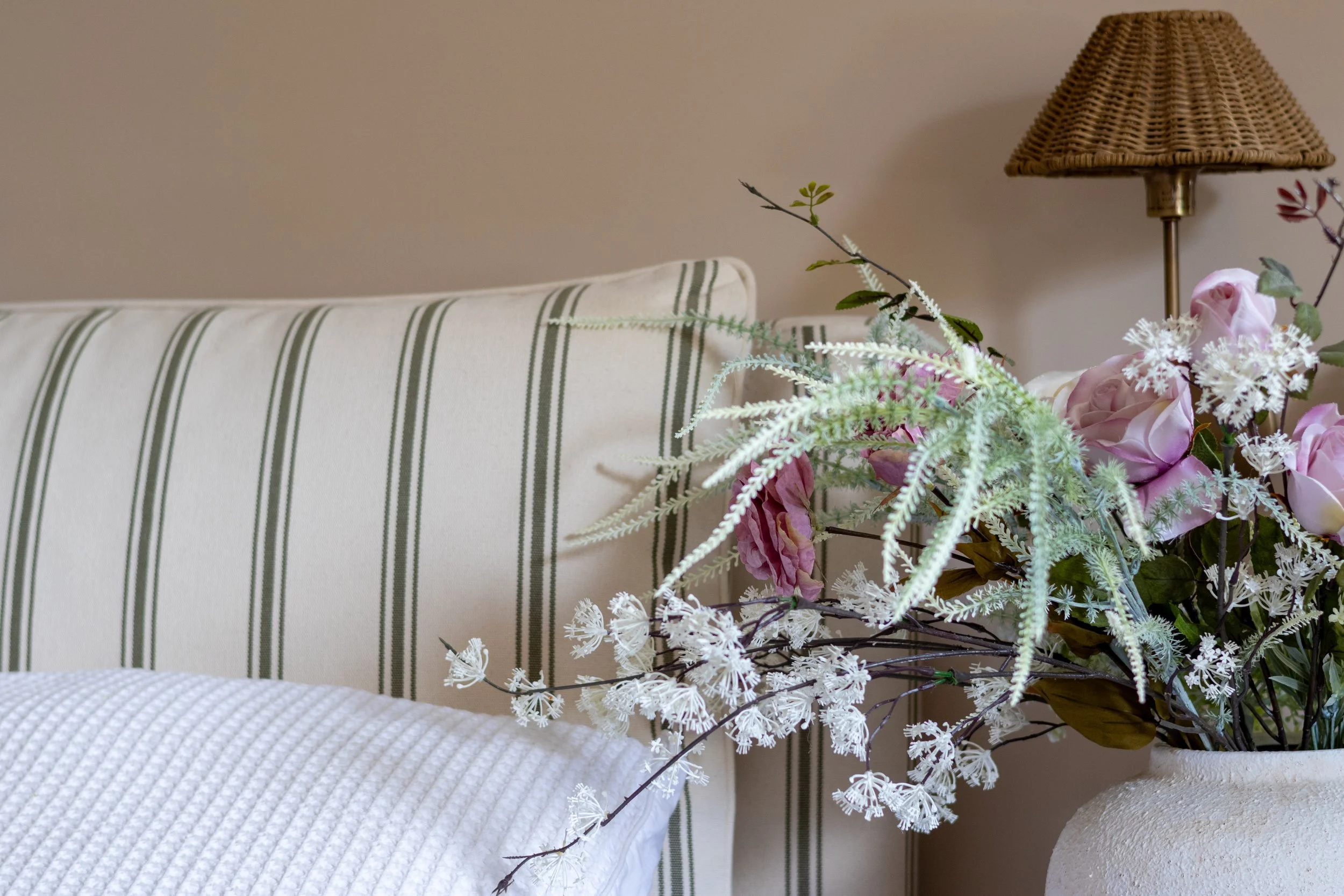 Pink roses and astilbe styled against a striped cream and olive cushion