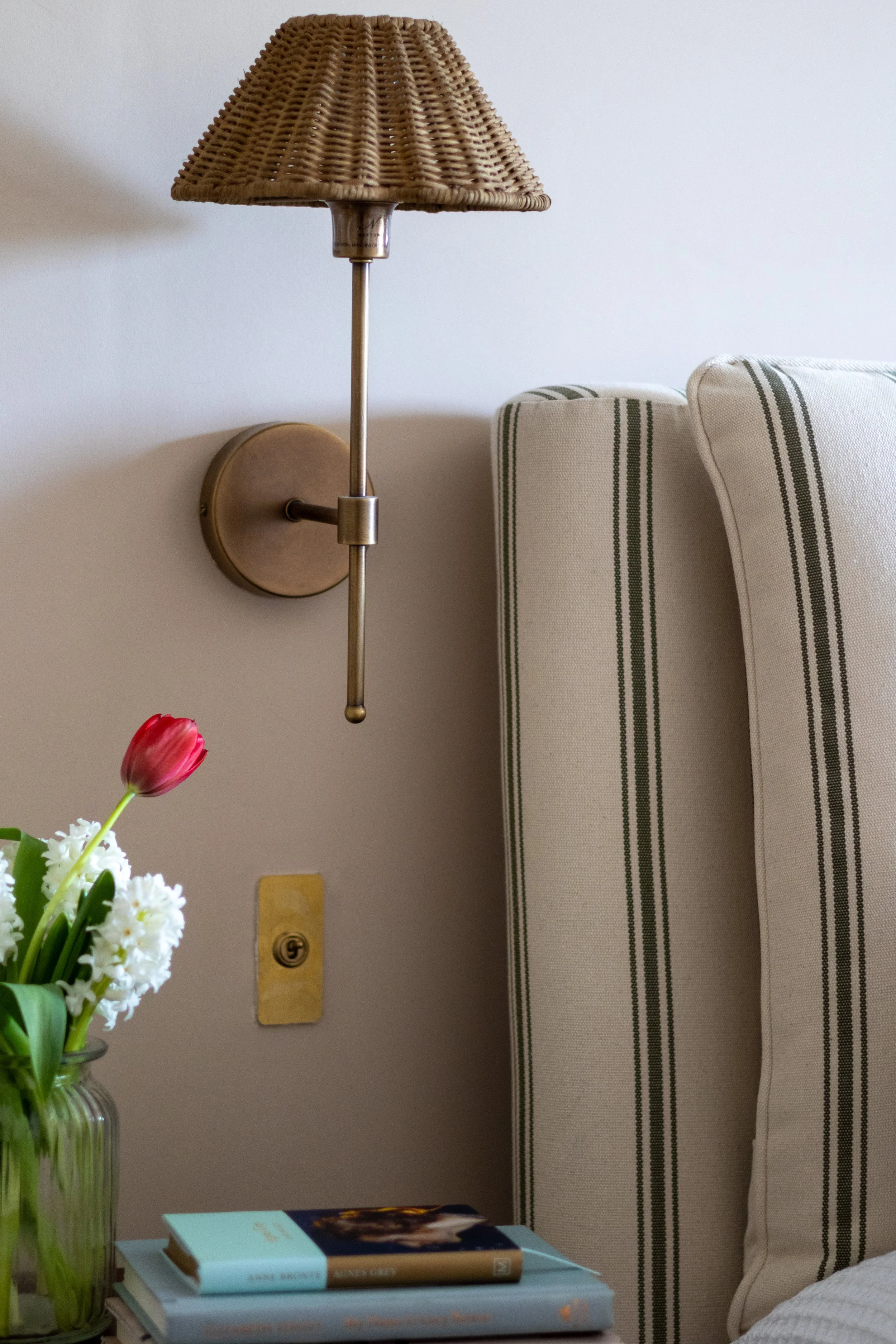 Woven rattan wall-mounted light fixture above a bedside table stacked with books