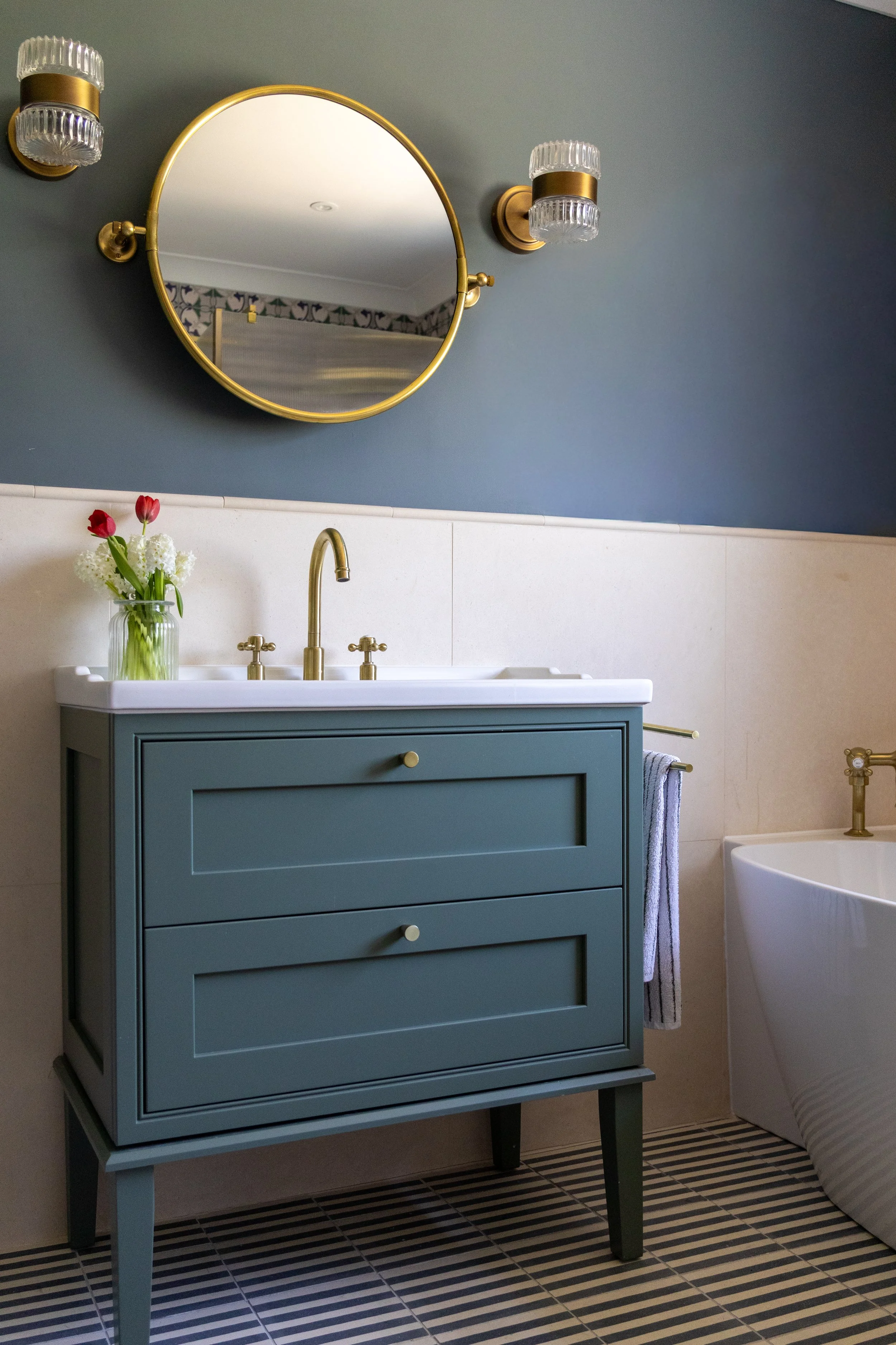 Teal shaker-style vanity unit with brass taps beneath a round brass-framed mirror