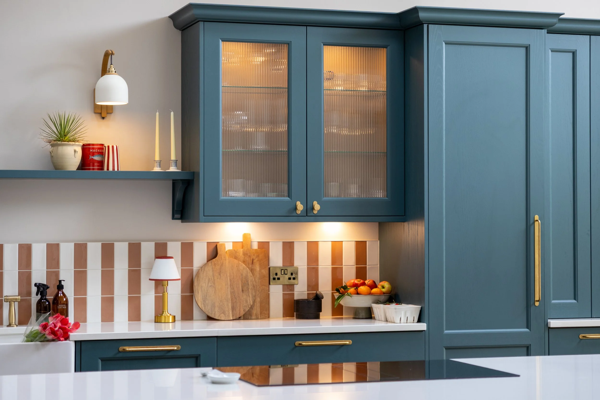 Teal glass-fronted wall cabinet above a terracotta and cream striped tile splashback
