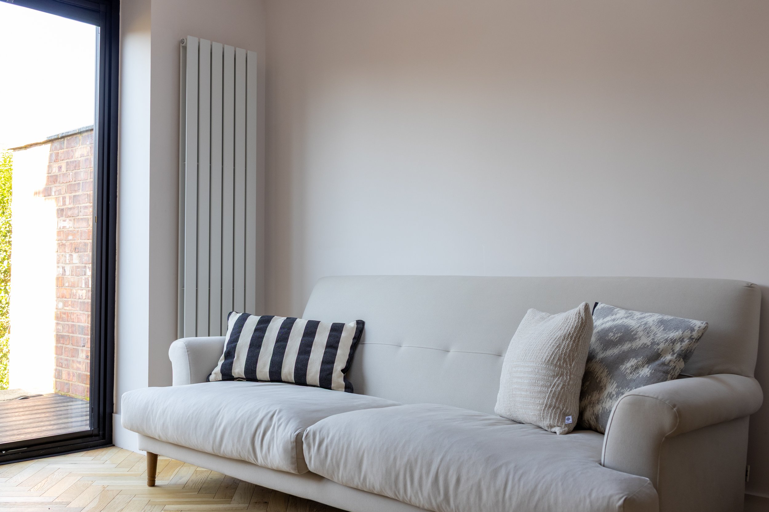 Pale grey sofa with striped and textured cushions beside a vertical radiator and bifold doors