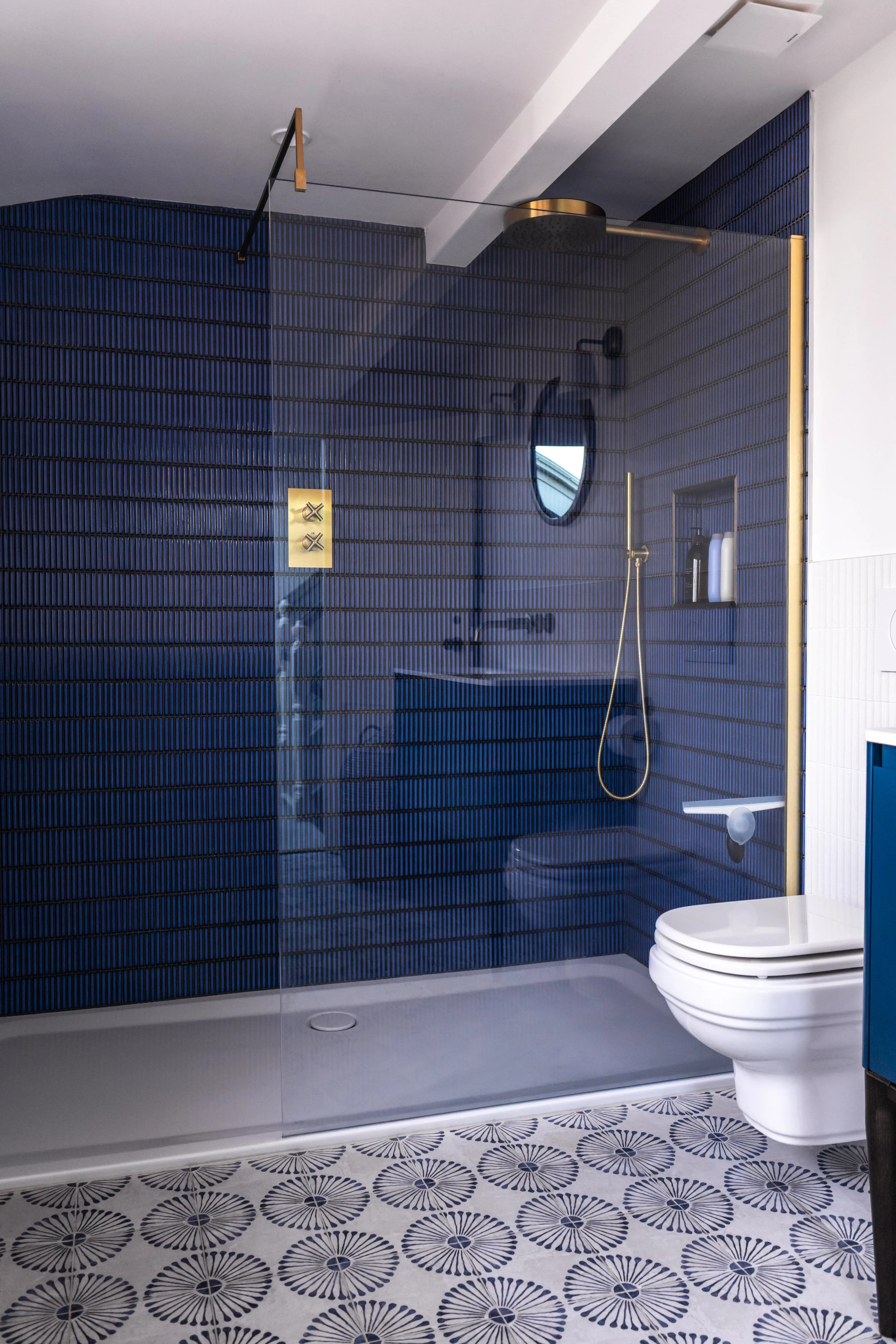 Navy ribbed-tile walk-in shower with glass screen, brass fittings and starburst-patterned floor