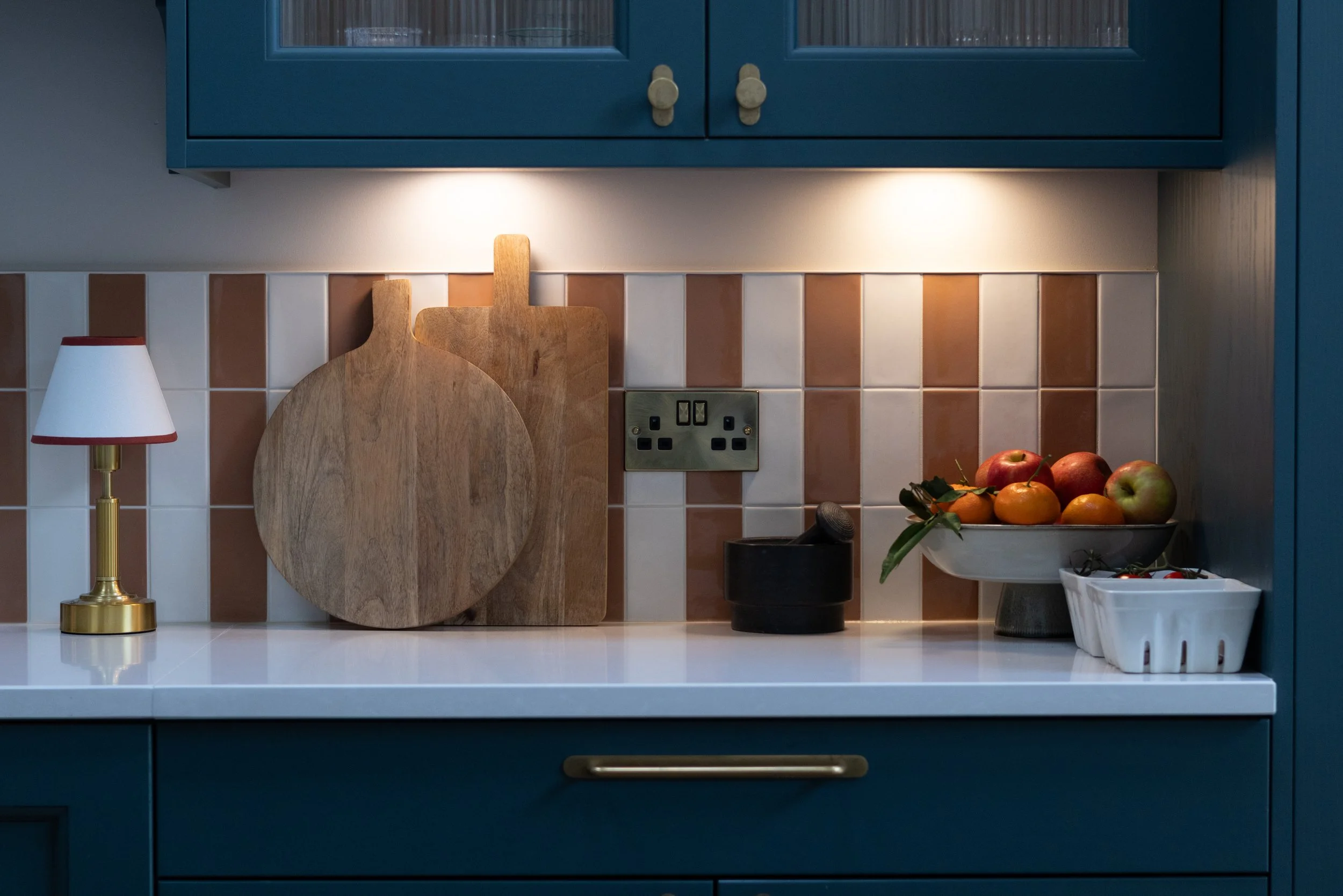 Wooden chopping boards leaning against terracotta striped tiles beside a fruit bowl