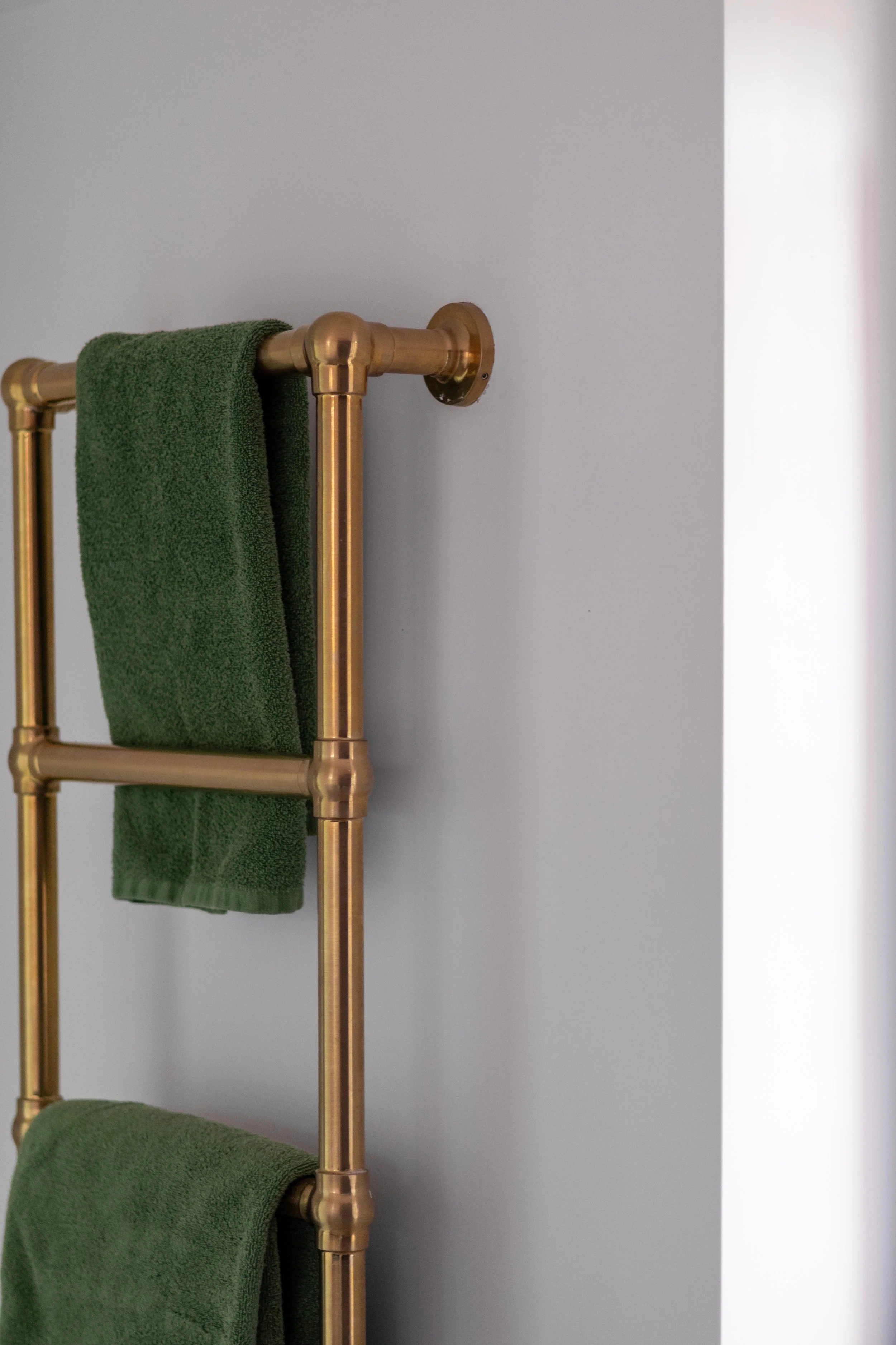 Brass ladder-style towel rail holding folded green towels against a grey wall