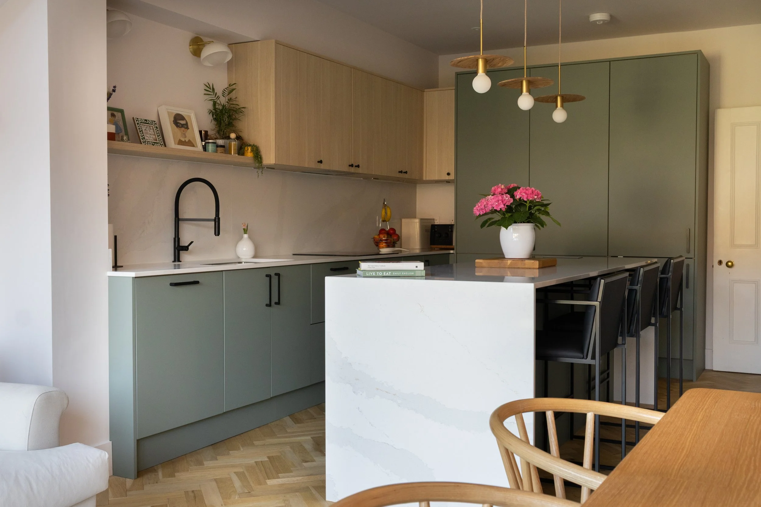 Open-plan sage green kitchen with island seating, pendant lighting and adjoining dining area