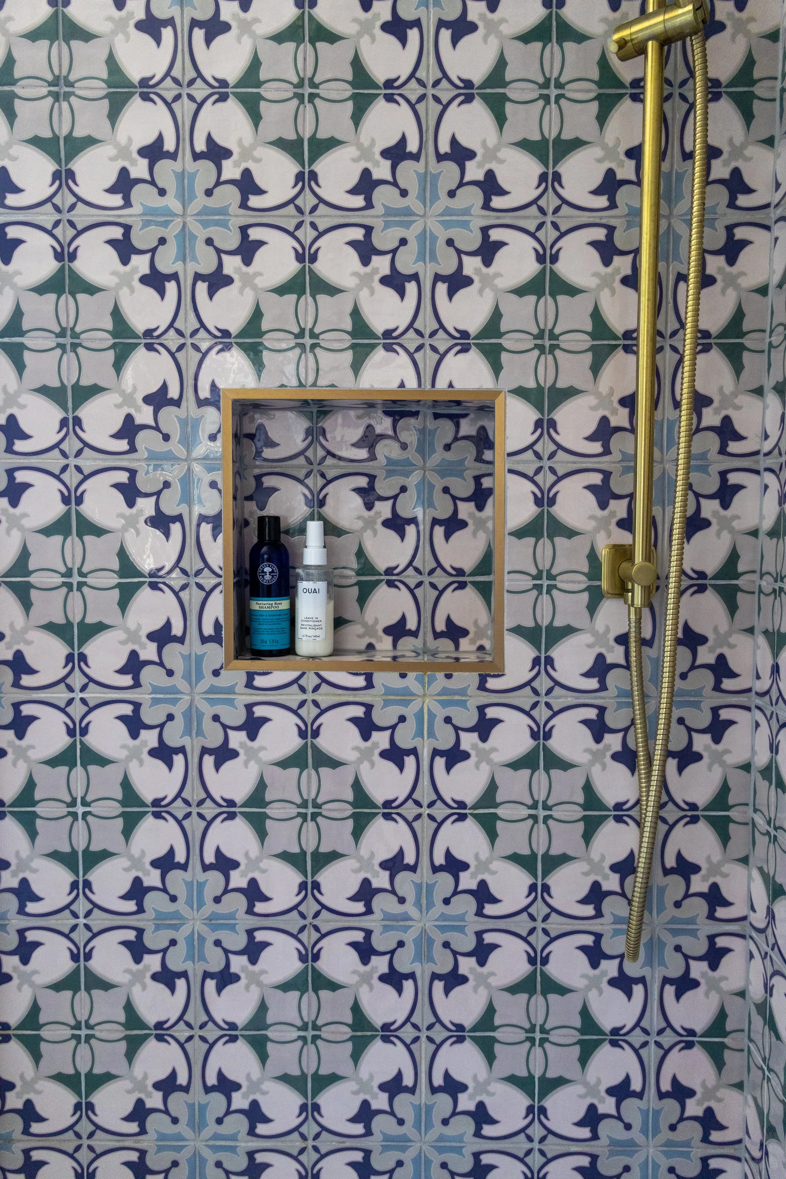 Blue and green Moroccan-style tiled shower wall with brass fitting and recessed storage niche