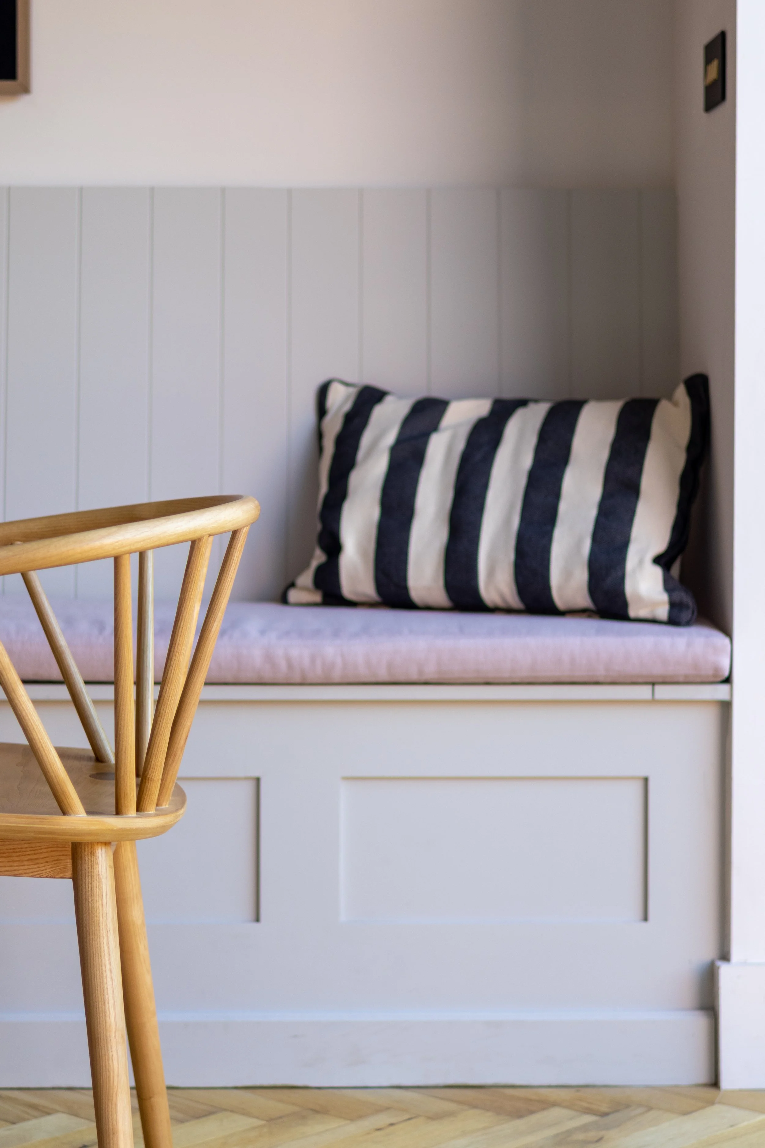 Oak Windsor-style chair beside a panelled bench seat with lilac cushion and striped bolster