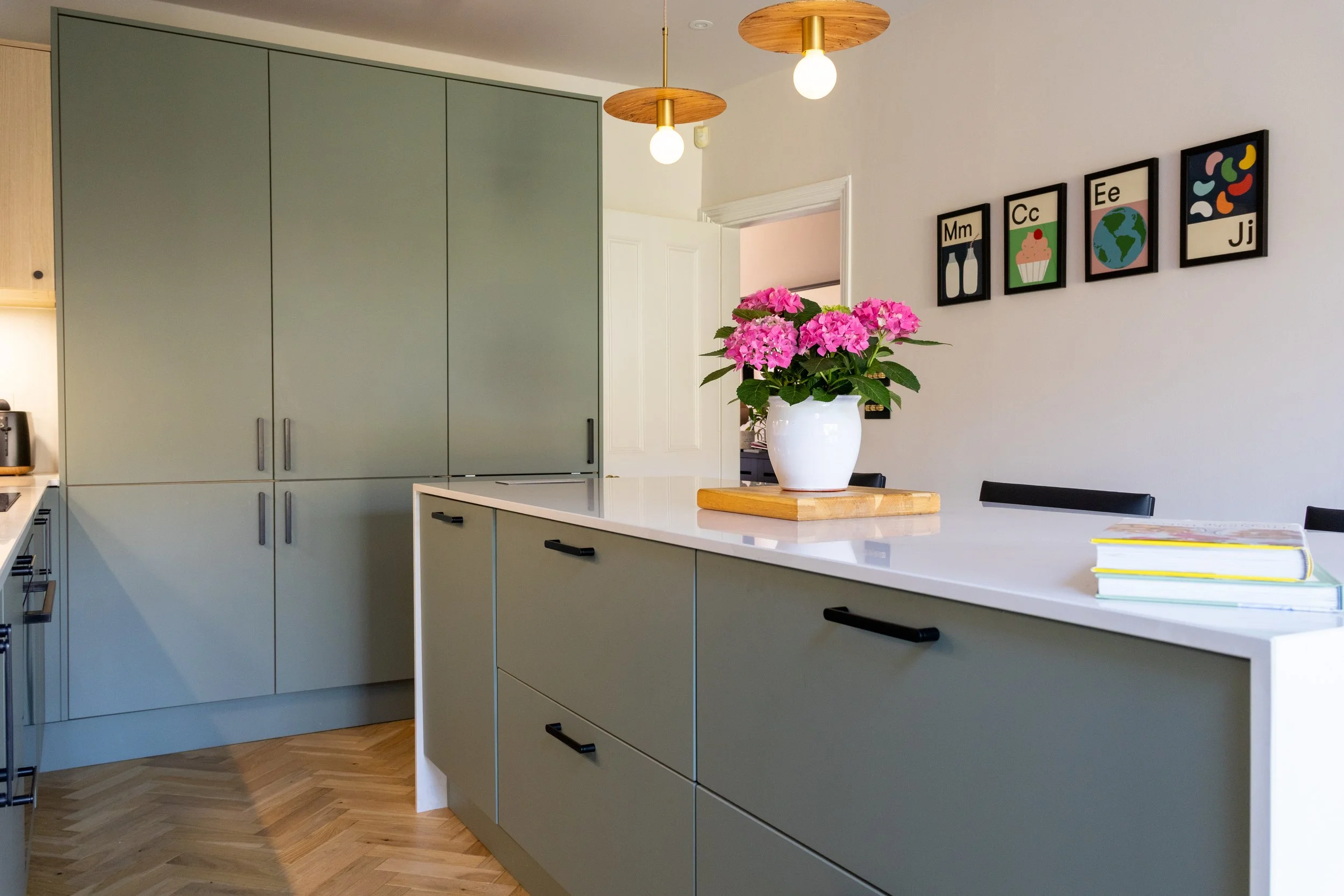 Sage green kitchen island with black bar handles beneath wood and brass disc pendant lights
