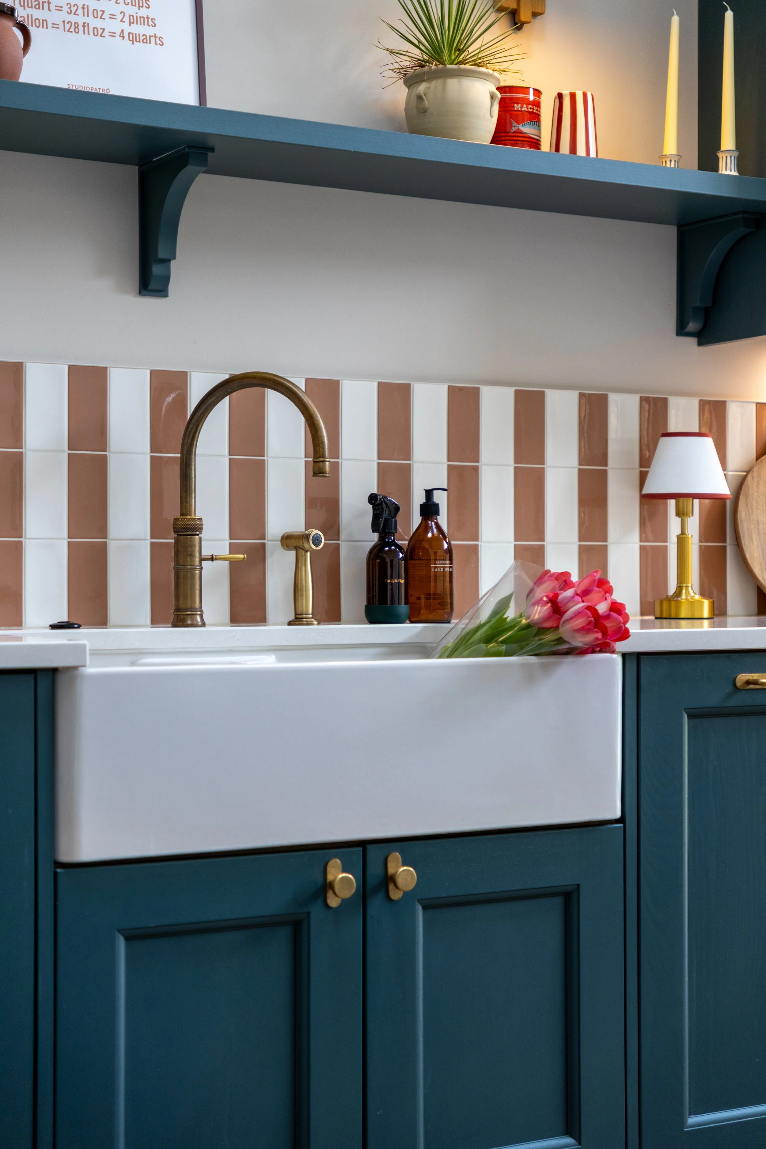White Belfast sink with brass tap below a striped tile splashback and open shelf styling