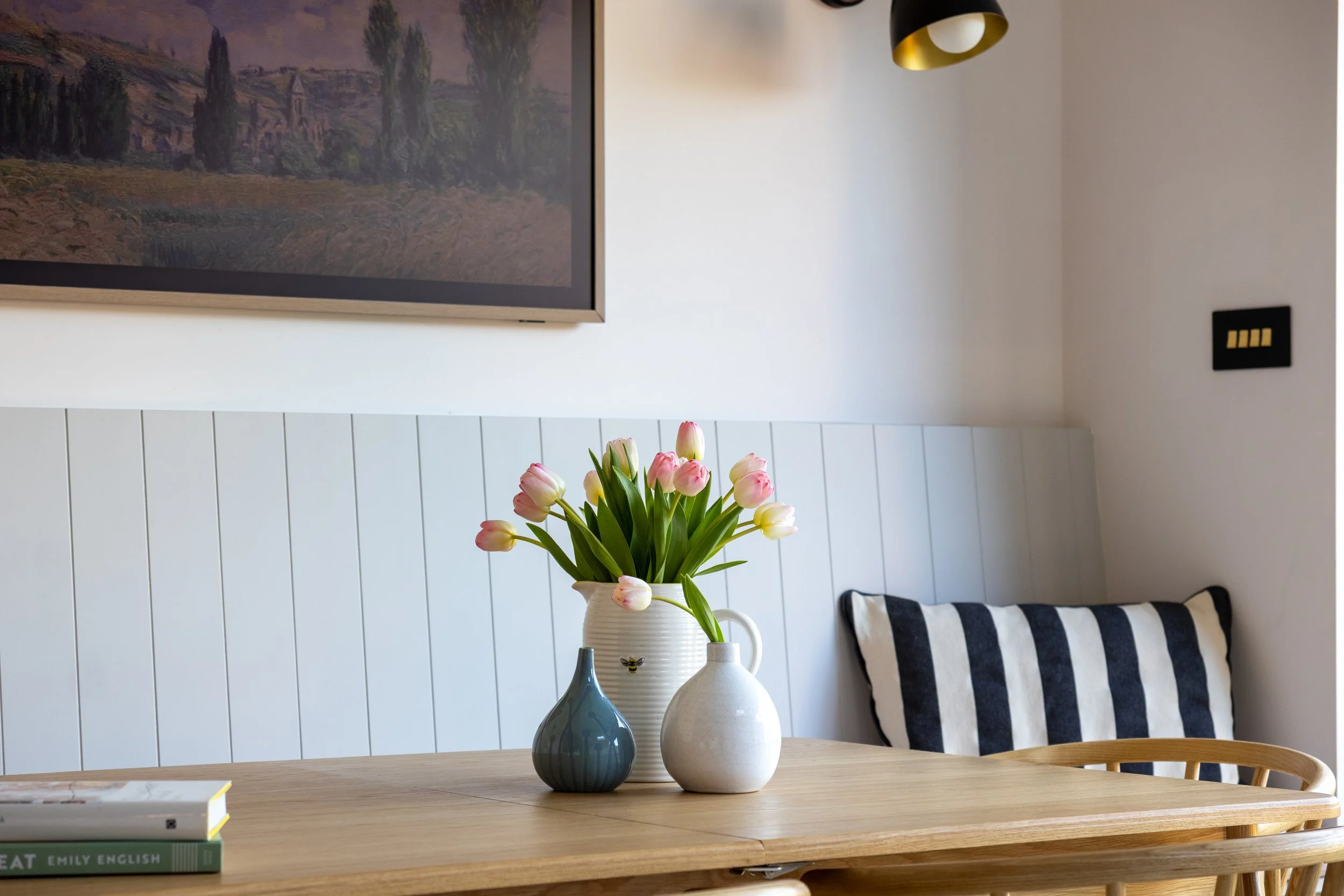 Oak dining table and Windsor chairs beneath framed landscape art and black-and-brass wall lights