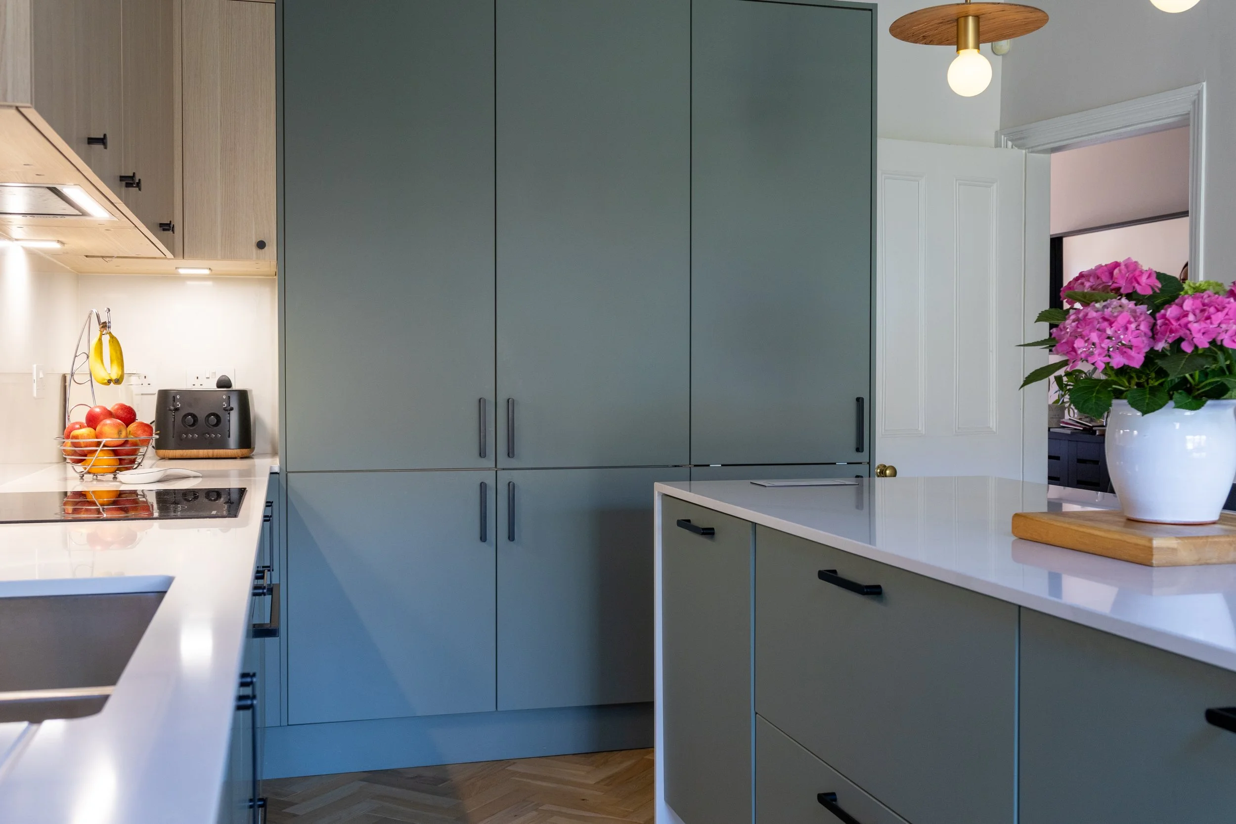 Blue-grey kitchen cabinetry with wire fruit basket, toaster and herringbone oak flooring