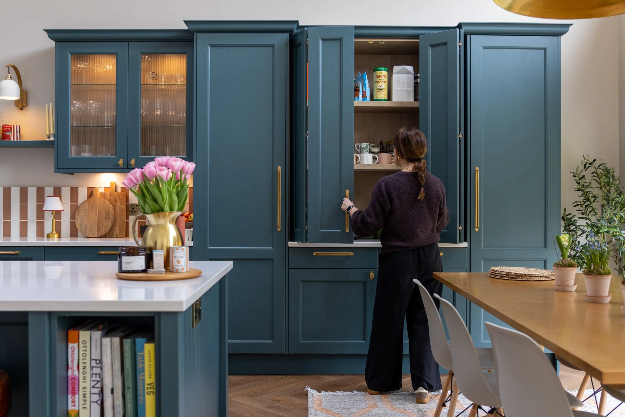 Woman reaching into a tall teal pantry cupboard stocked with jars and kitchen storage