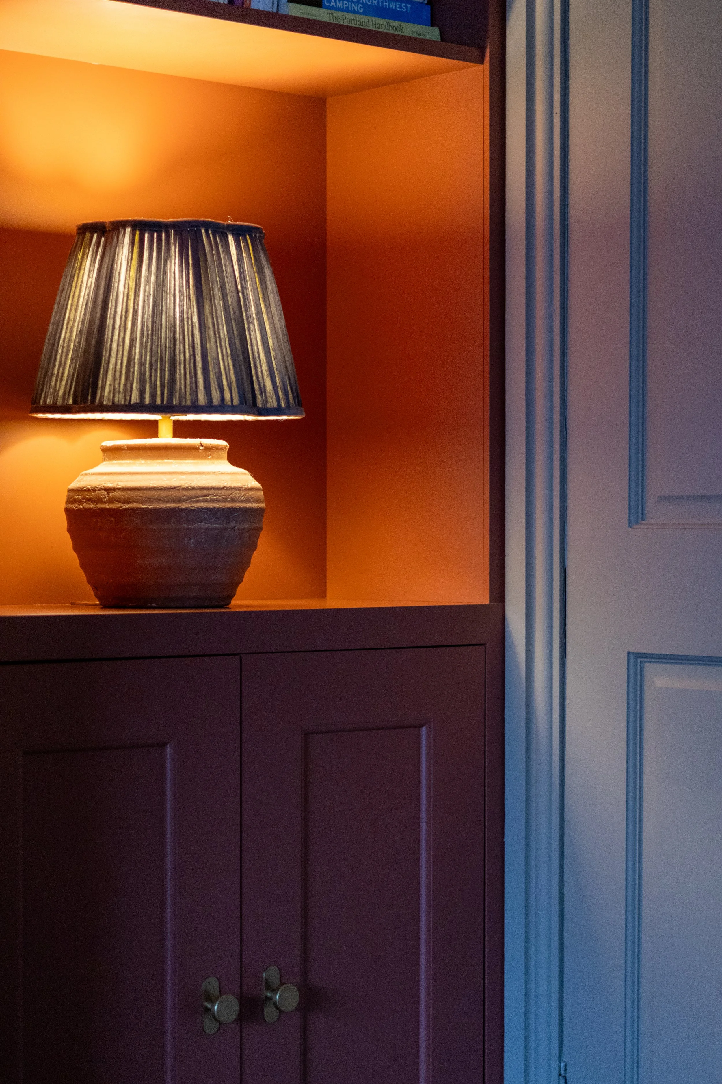 Terracotta ceramic lamp with pleated shade lit within a built-in orange-toned alcove