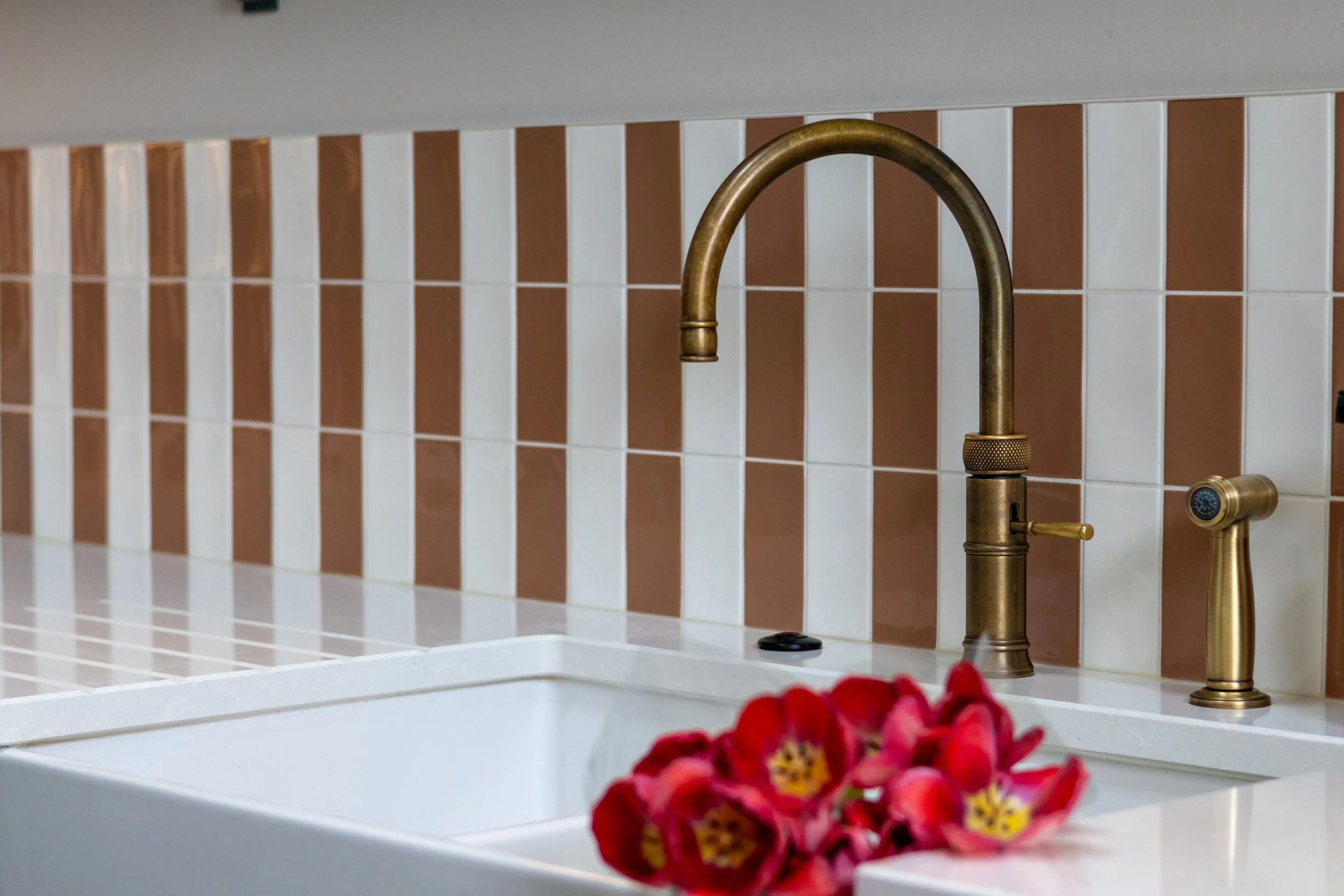Antique brass kitchen tap against terracotta striped tiles with red tulips in the foreground