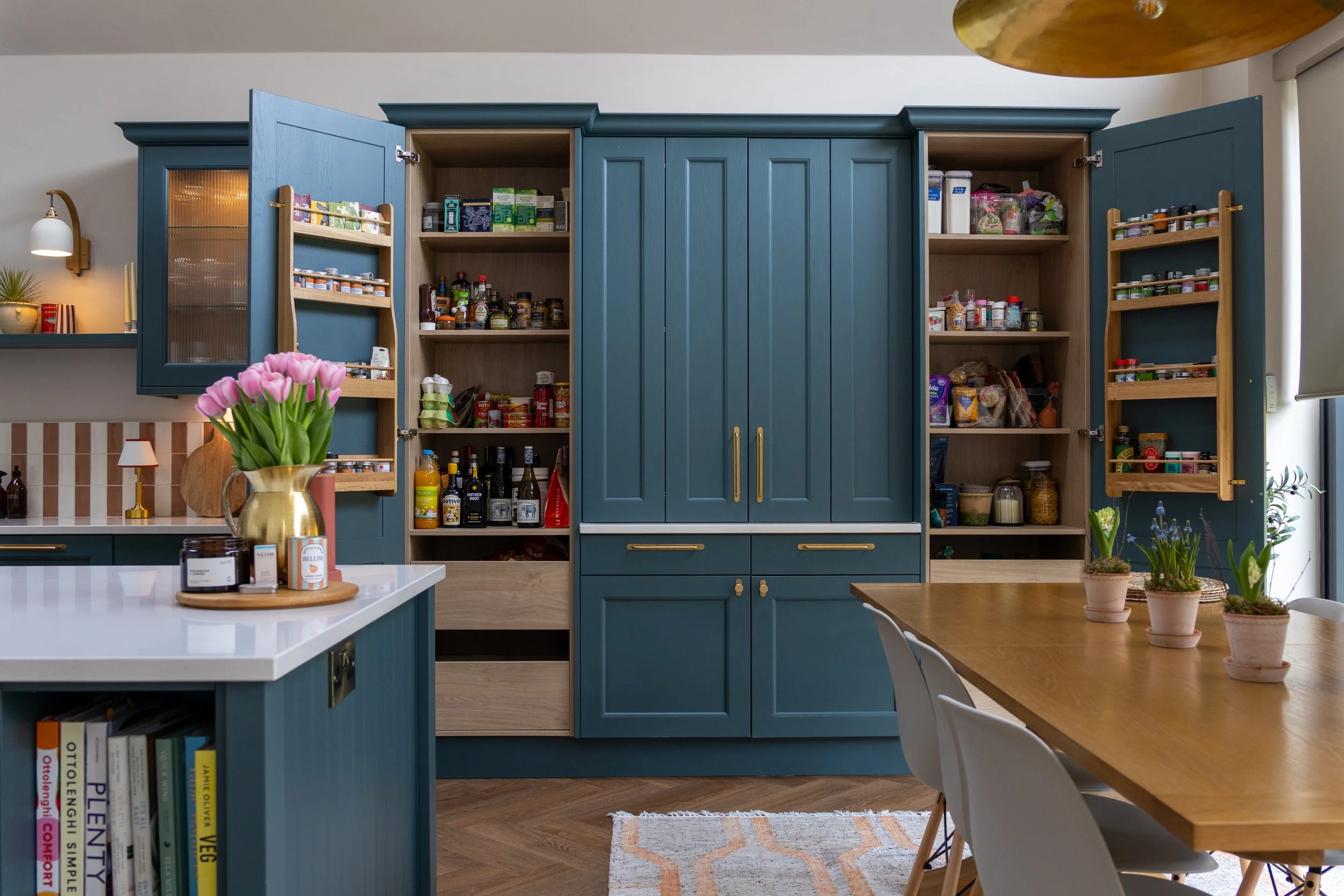 Dark teal pantry cupboard open to reveal shelved spice racks, jars and bottles