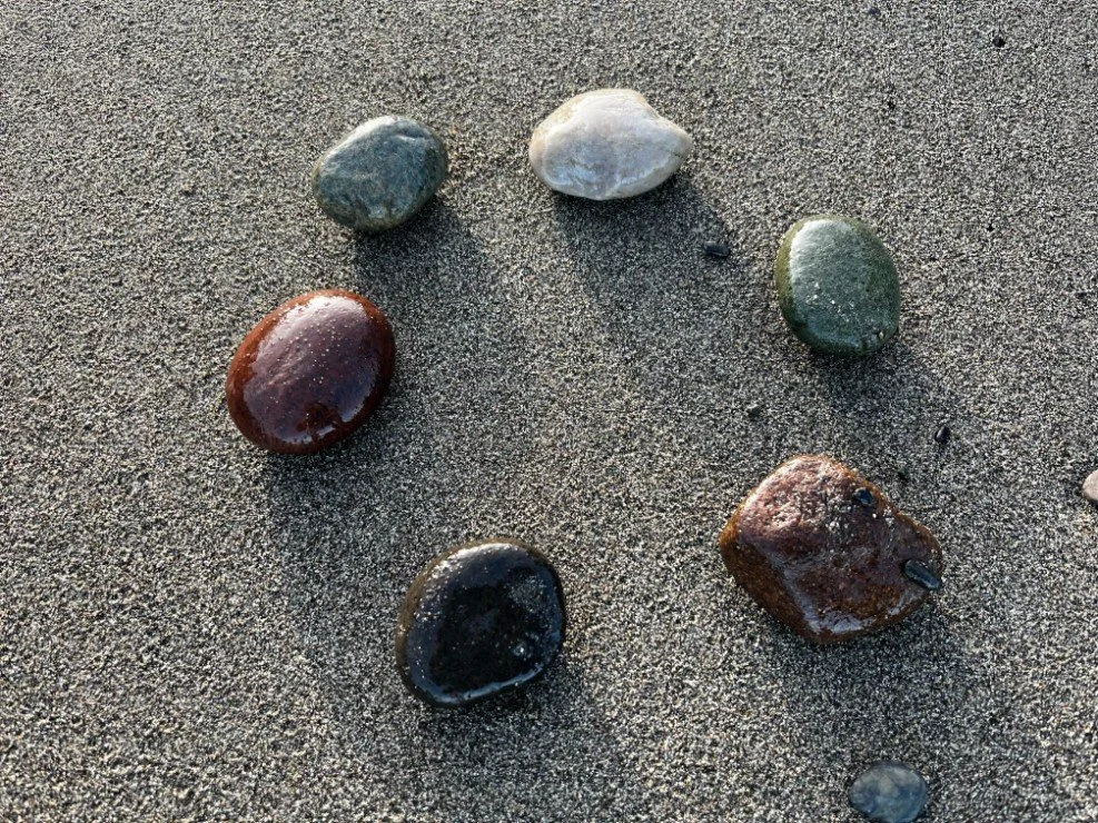 Six colorful, smooth stones arranged in a circle on sandy ground.