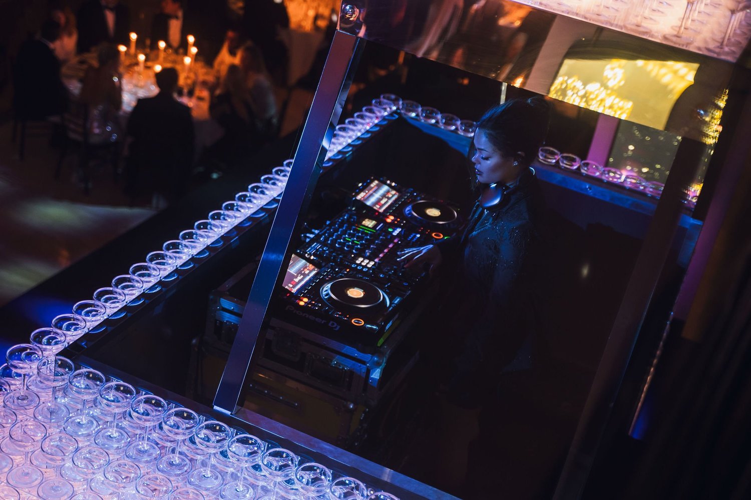 DJ performing behind a booth lined with champagne glasses